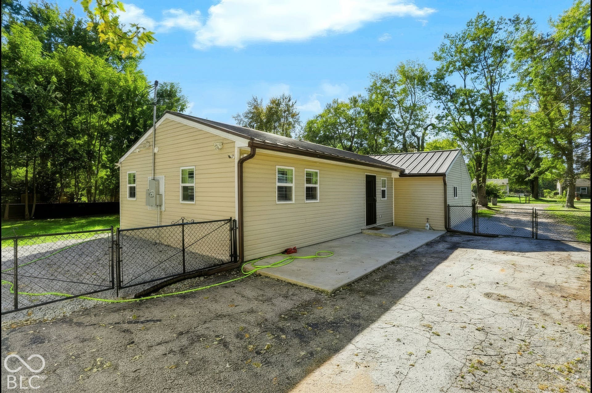 Light-colored siding exterior with multiple windows, a brown metal roof, and a concrete patio