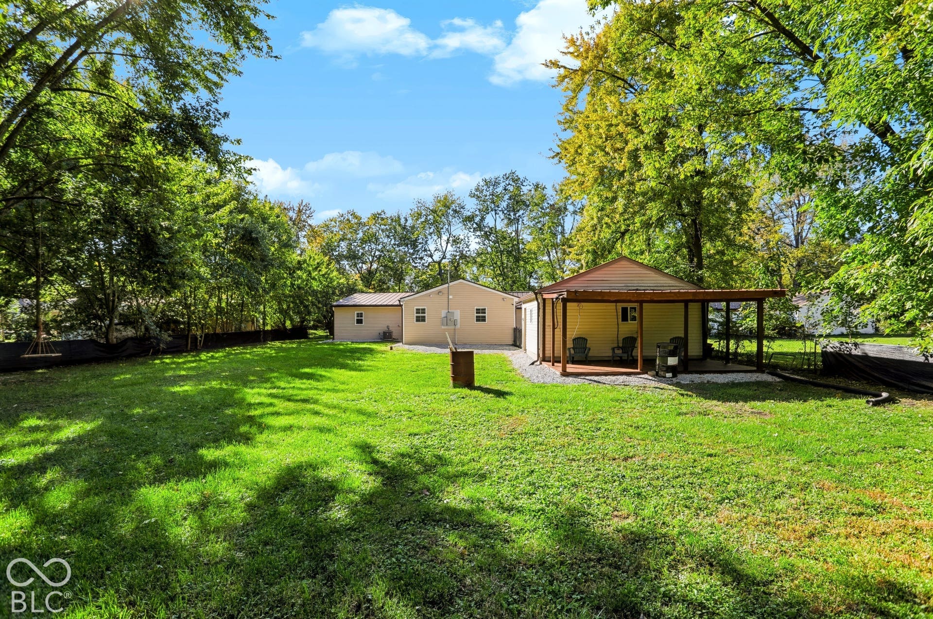Expansive backyard featuring a manicured lawn, established perimeter trees, and a covered patio with a wood-finish deck