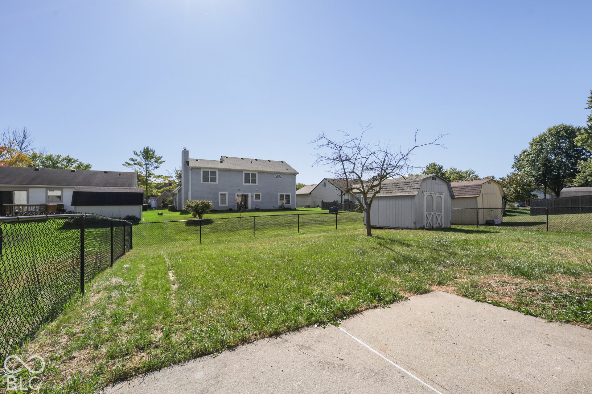 Expansive lawn with a black chain-link fence, a concrete patio, and a storage shed