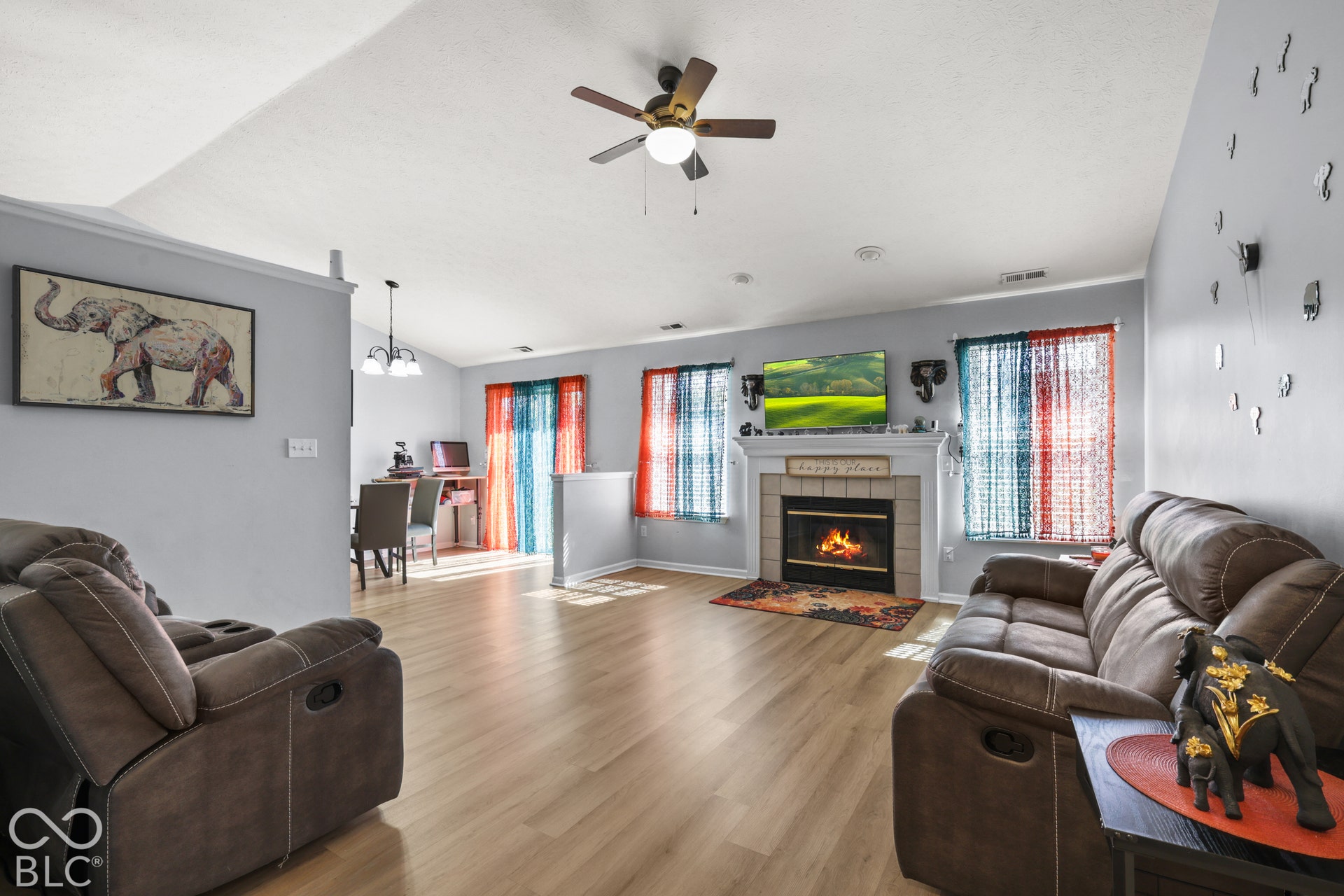 Vaulted ceiling with a ceiling fan, wood-finish flooring, and a fireplace with a mantel