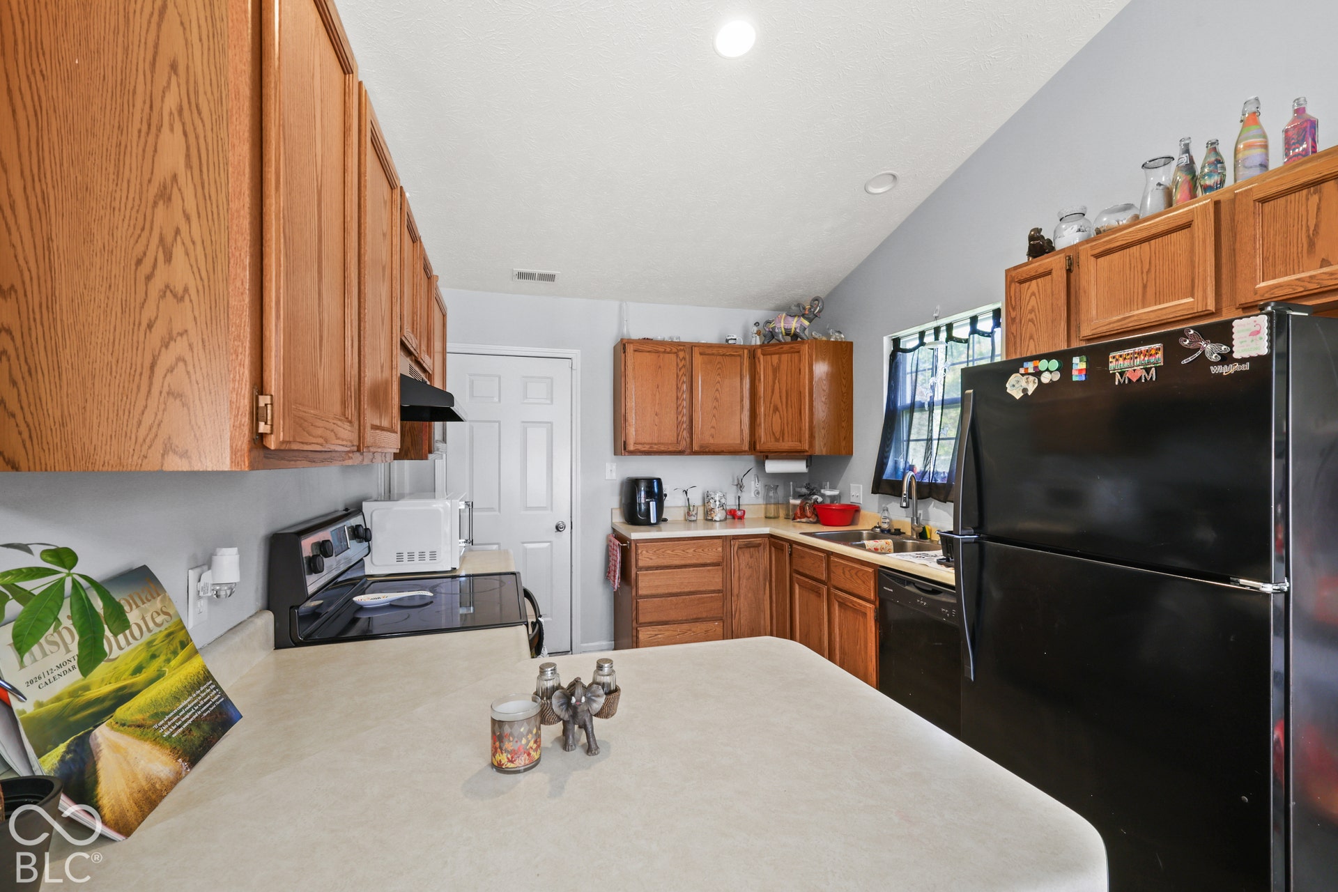 Wood-finish cabinetry, black appliances, light-toned countertops, and recessed lighting