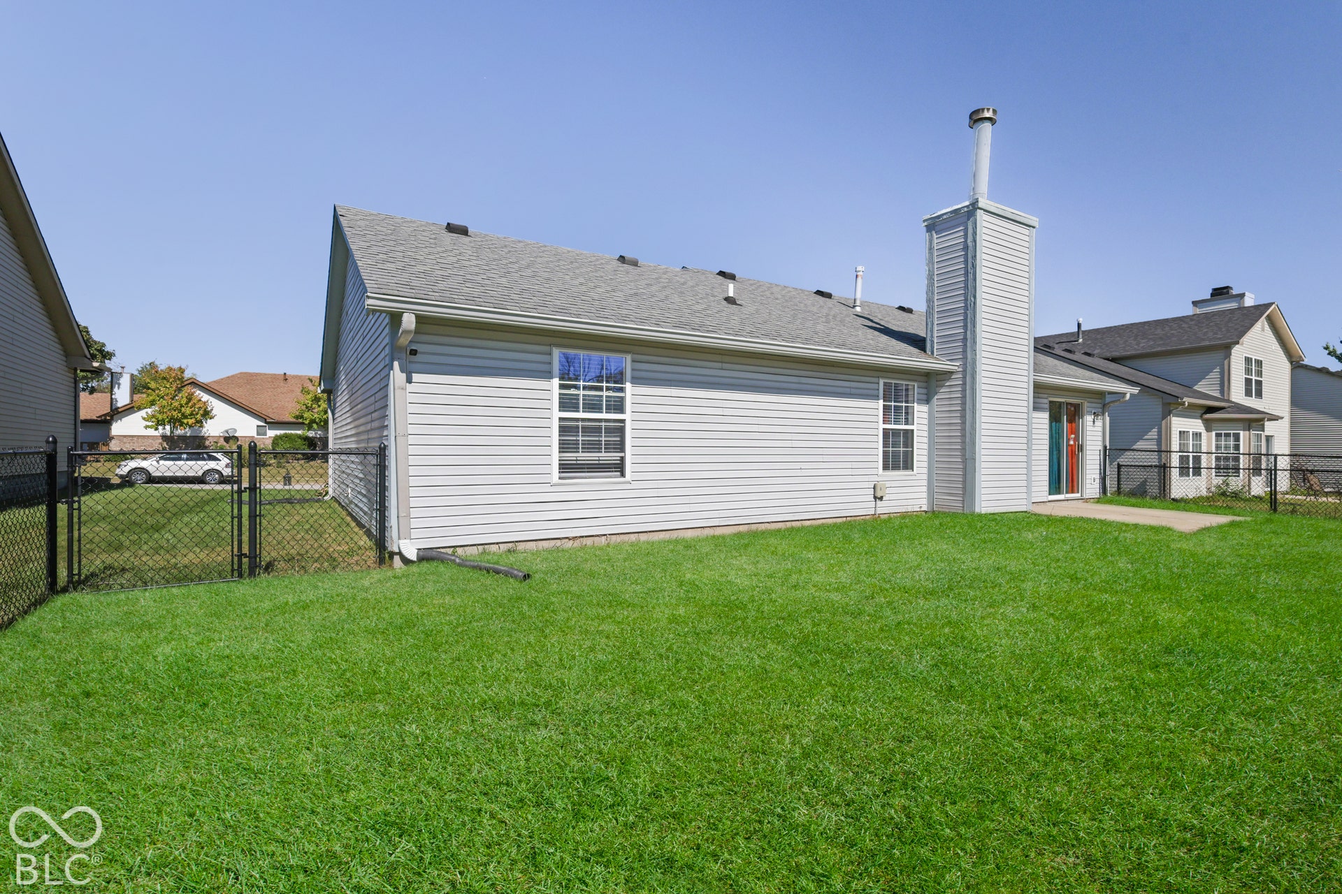 Expansive grassy yard with chain-link fencing, a concrete patio, and light-colored siding