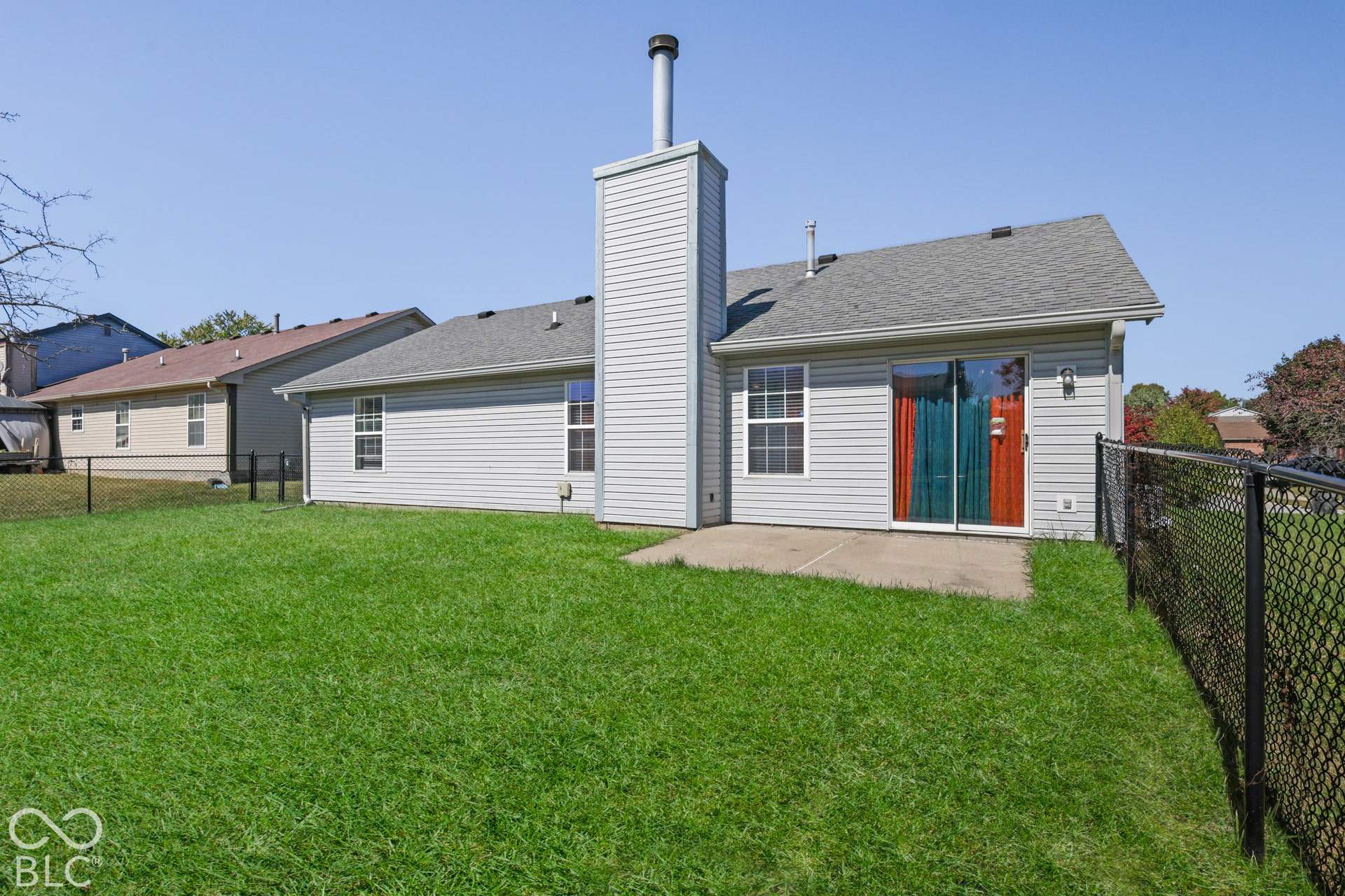 Expansive backyard featuring a manicured lawn, concrete patio, and a chain-link fence