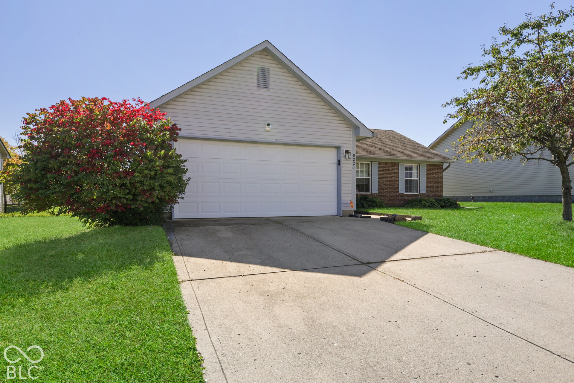 Two-car garage, concrete driveway, brick and siding exterior, front yard landscaping, mature trees