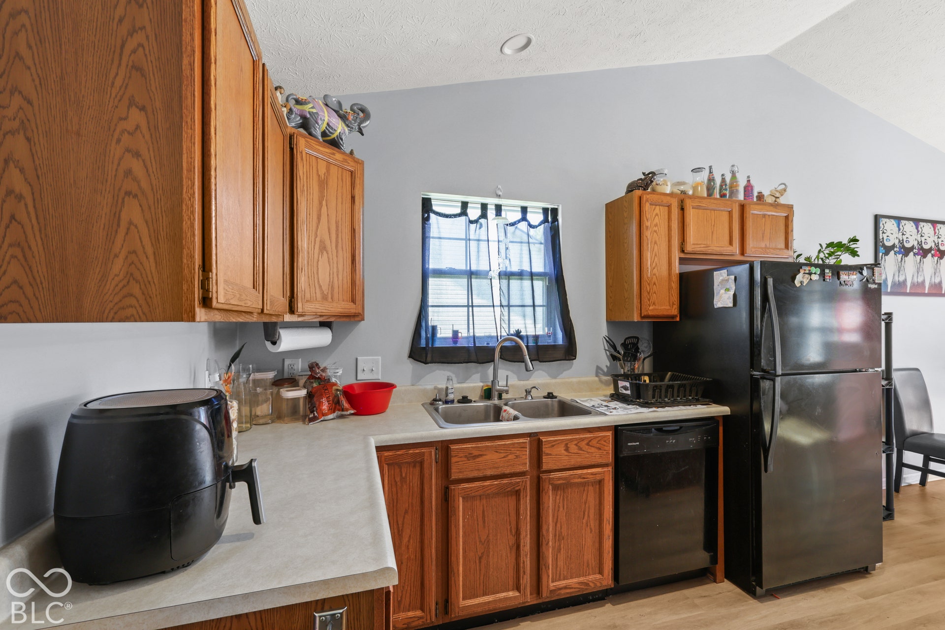 Kitchen featuring wood cabinetry, a double basin sink, black appliances, and vaulted ceilings