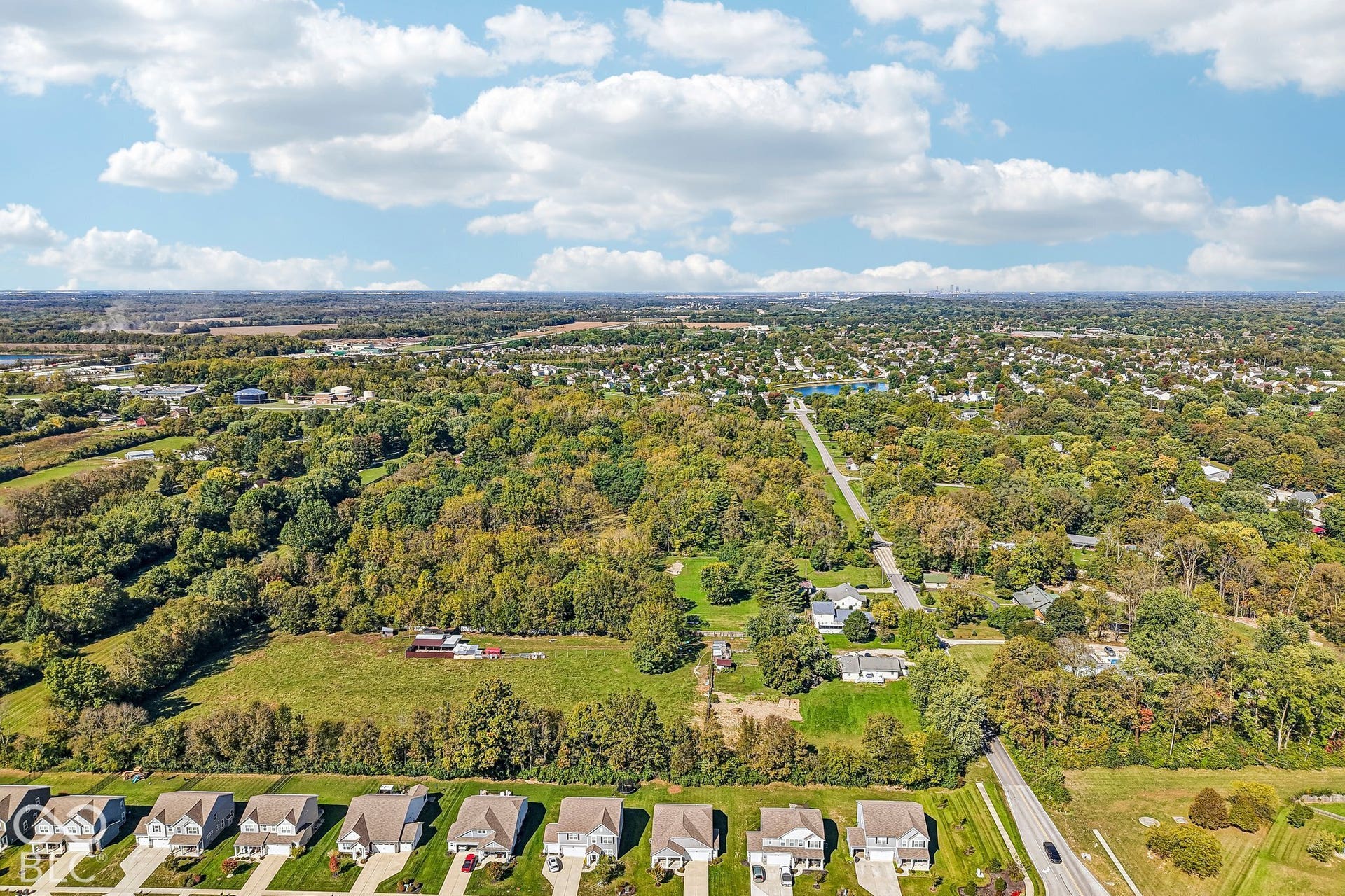 Expansive aerial view showcasing residential areas, abundant mature trees, and a distant body of water