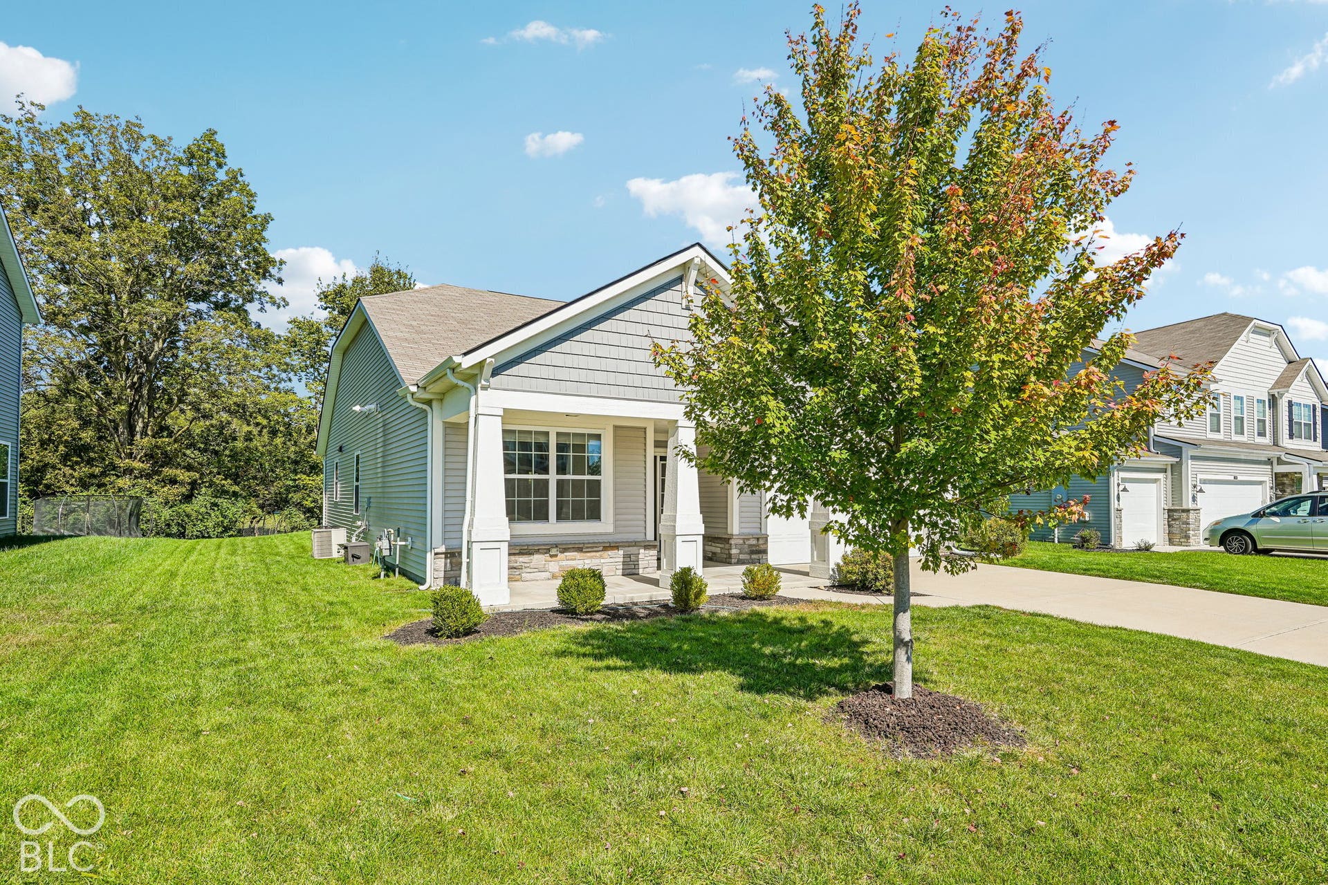 Light gray siding exterior with shake accents, a covered front porch with stone base pillars, and a mature tree in the front yard