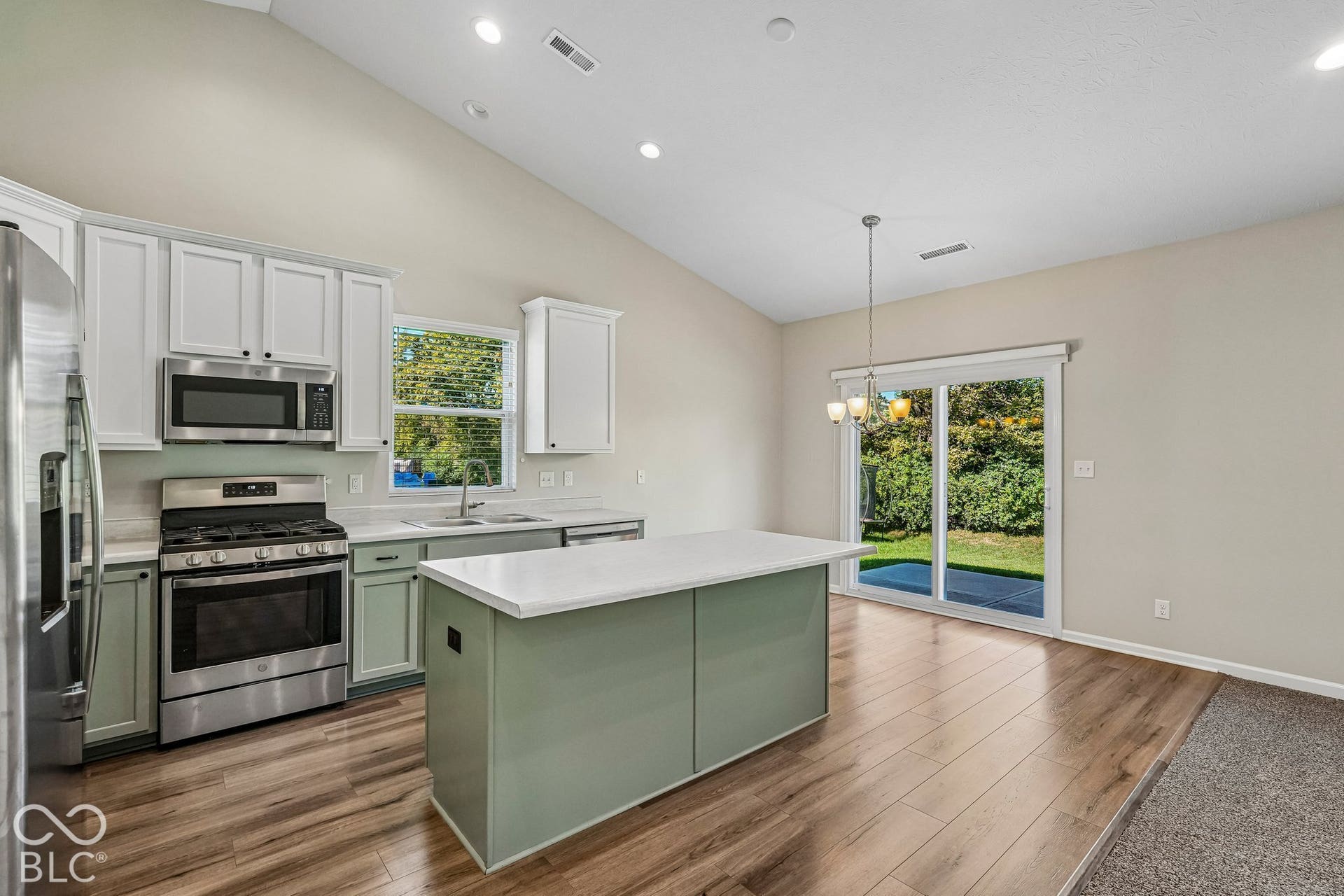 Vaulted ceilings with recessed lighting, stainless steel appliances, wood-finish flooring, kitchen island with solid surface countertop, and sliding glass door