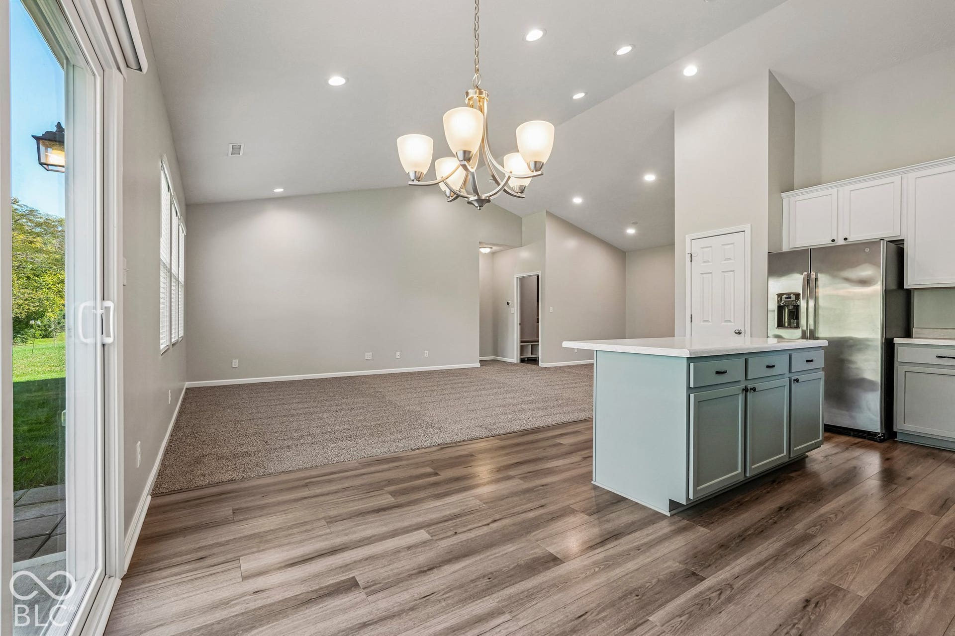 Vaulted ceilings, recessed lighting, and wood-finish flooring complement the central kitchen island with a white countertop