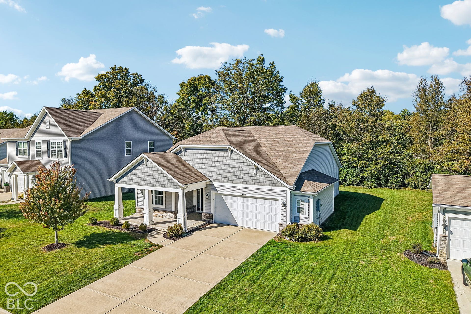 Exterior featuring a covered porch with stone accents, attached garage, well-maintained lawn, and mature trees