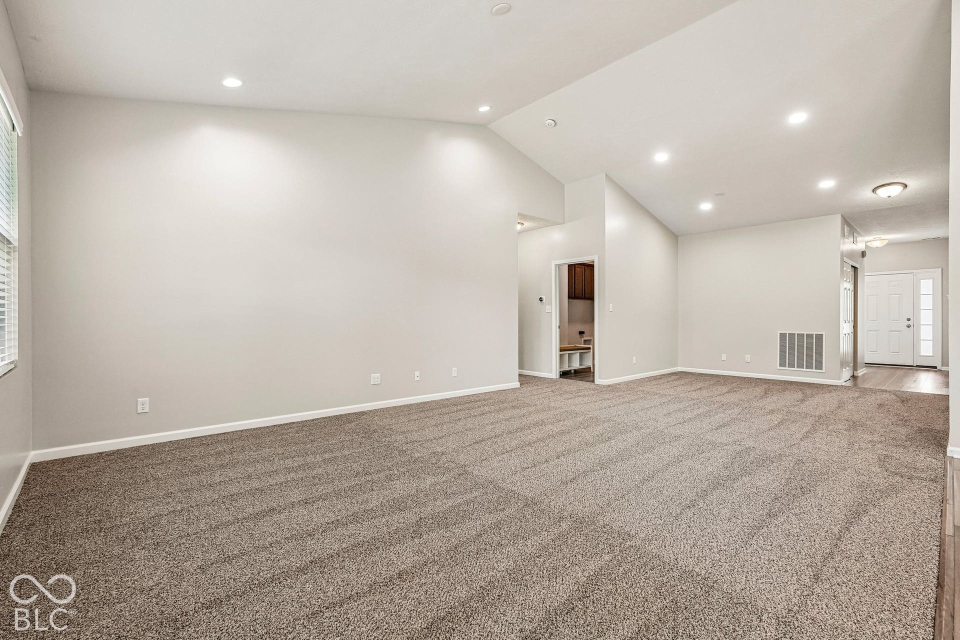 Expansive carpeted room featuring vaulted ceilings, recessed lighting, and neutral wall tones