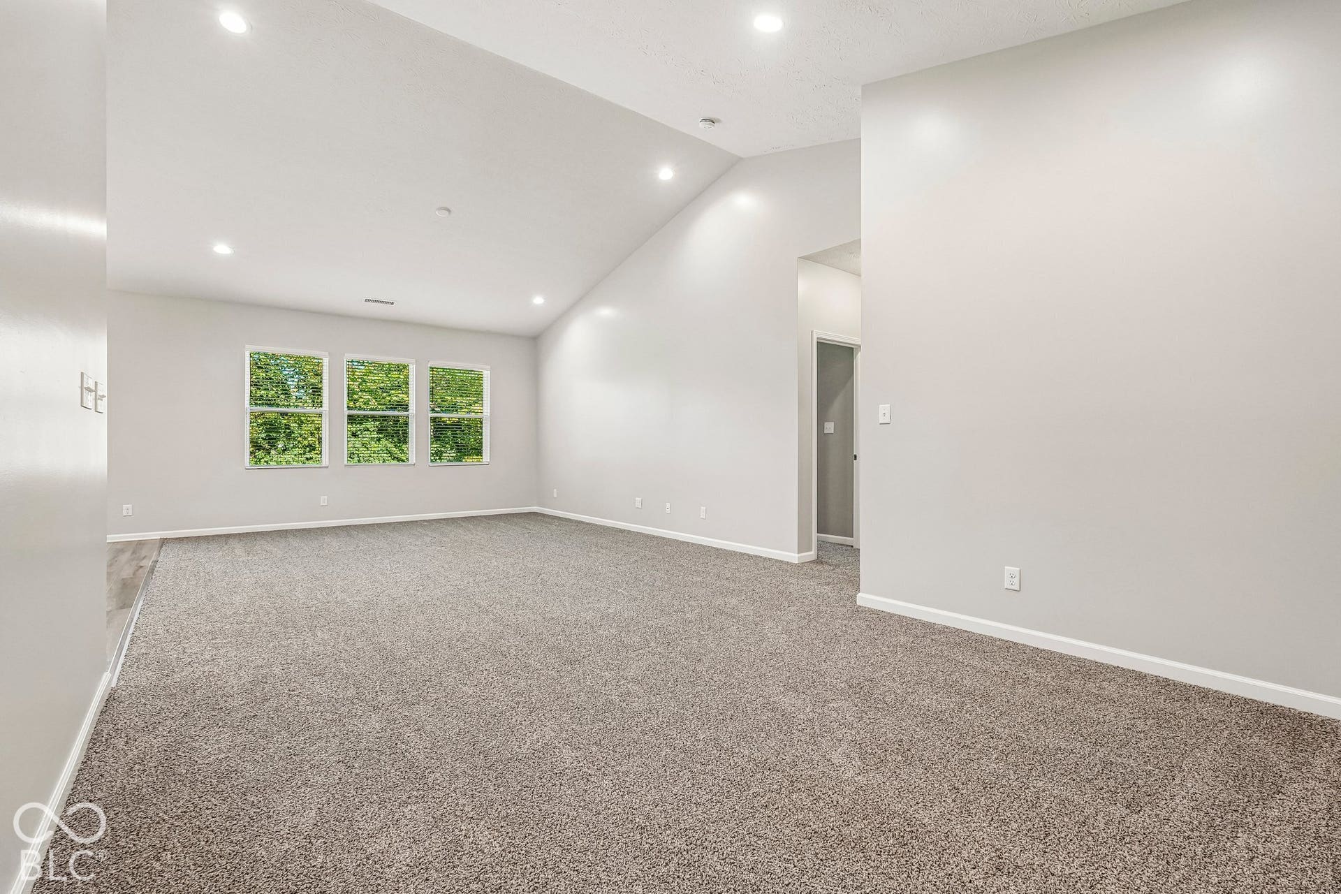 Vaulted ceiling with recessed lighting, three windows, light gray wall paint, and gray carpet