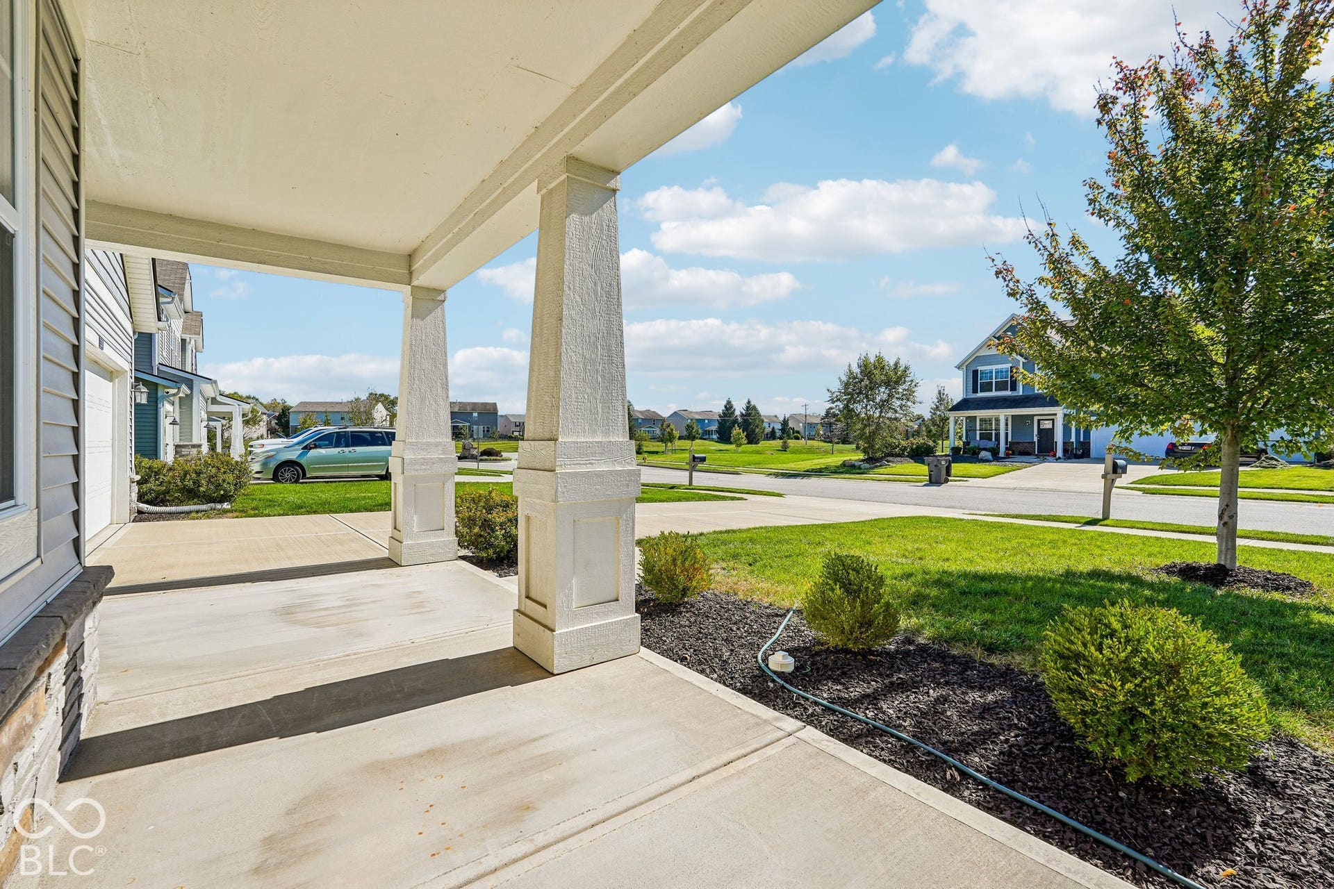 Covered concrete porch with decorative pillars, stone facade detailing, and adjacent landscaping