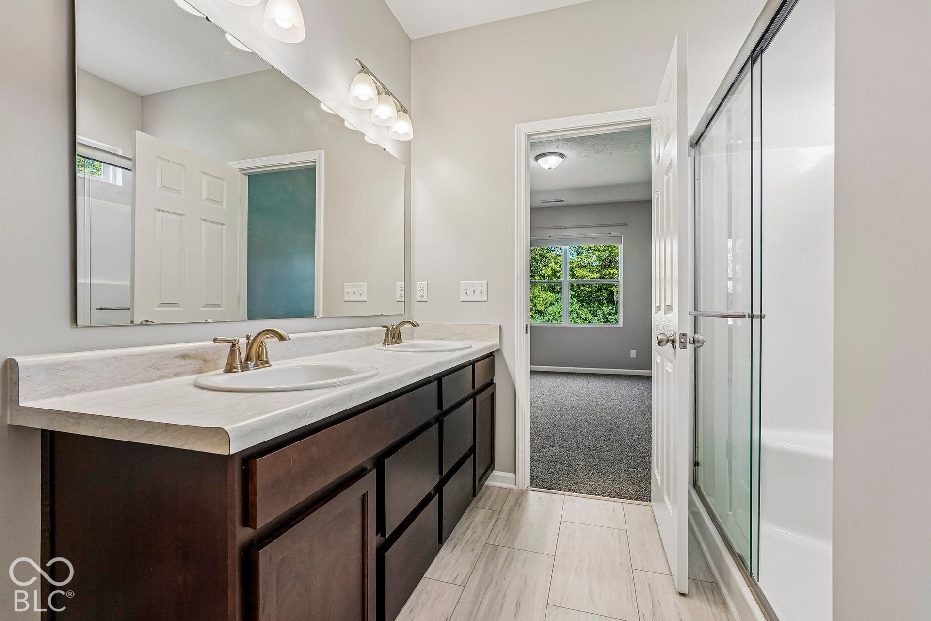 Dual vanity with undermount sinks, wood-finish cabinetry, and a large wall-mounted mirror