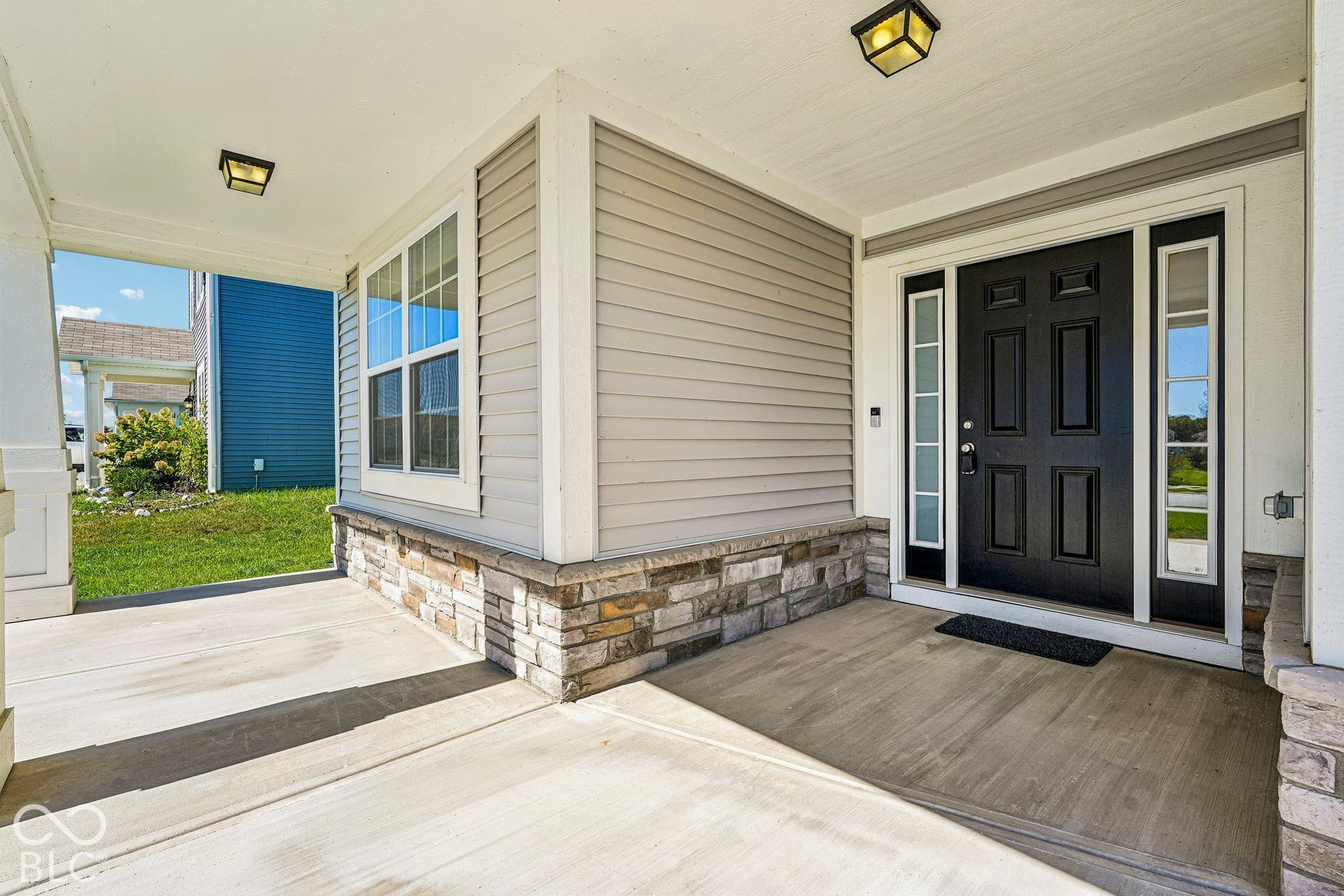 Covered front entry featuring a paneled black door with transom windows, sidelights, and overhead lighting