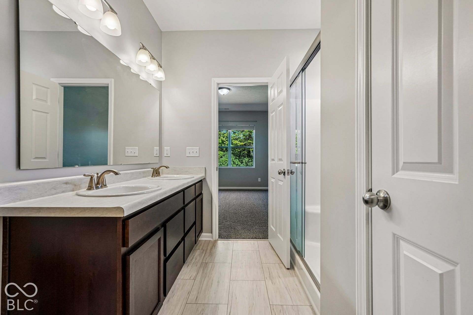 Dual vanity with white countertop and integrated sinks, wood-finish cabinetry, brushed nickel hardware, and tile flooring