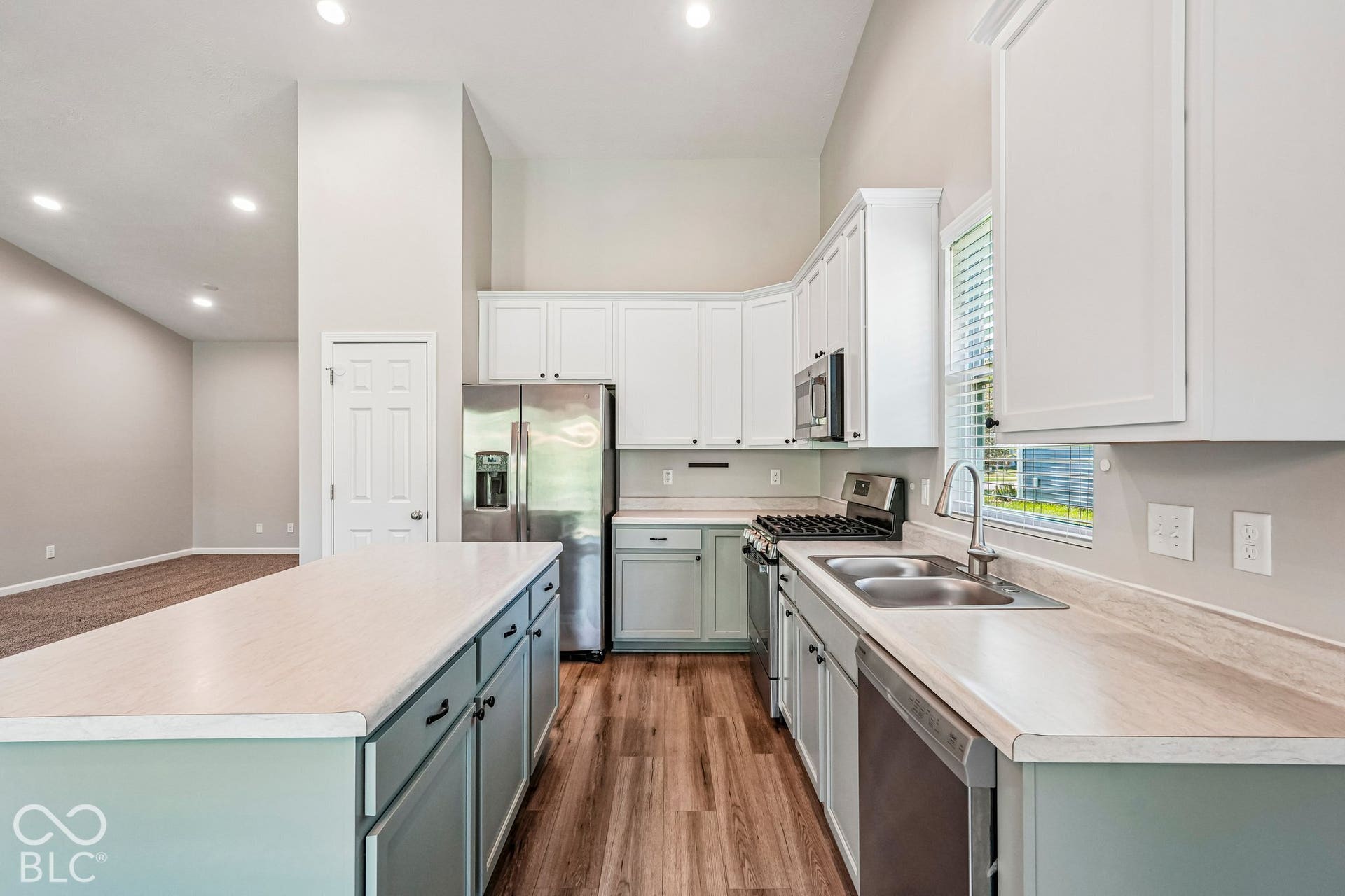 Kitchen featuring wood-finish flooring, two-tone cabinetry, stainless steel appliances, a dual basin sink, and an expansive island with countertop seating