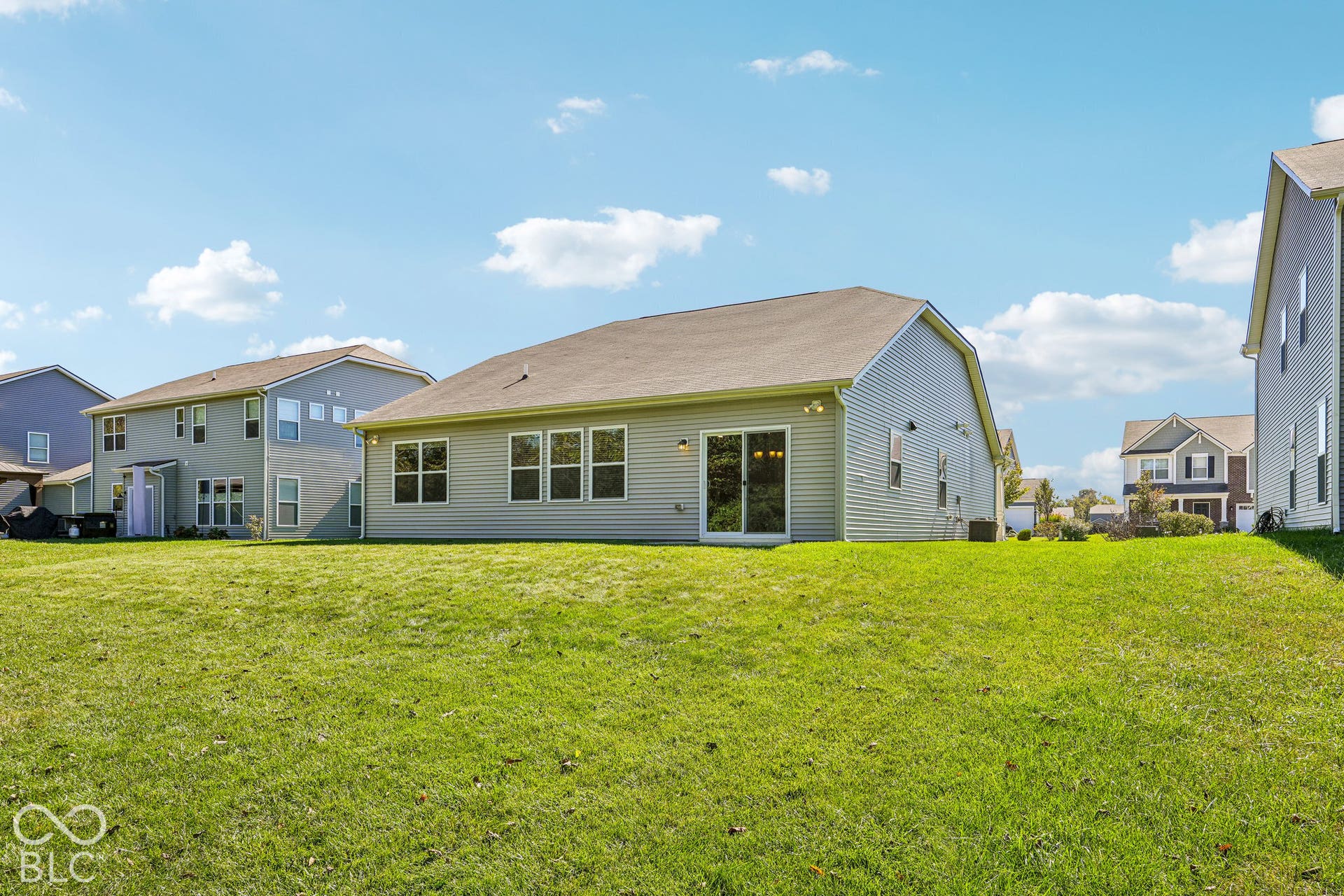 Expansive green lawn with a two-story residence featuring light-colored siding and a sliding glass door