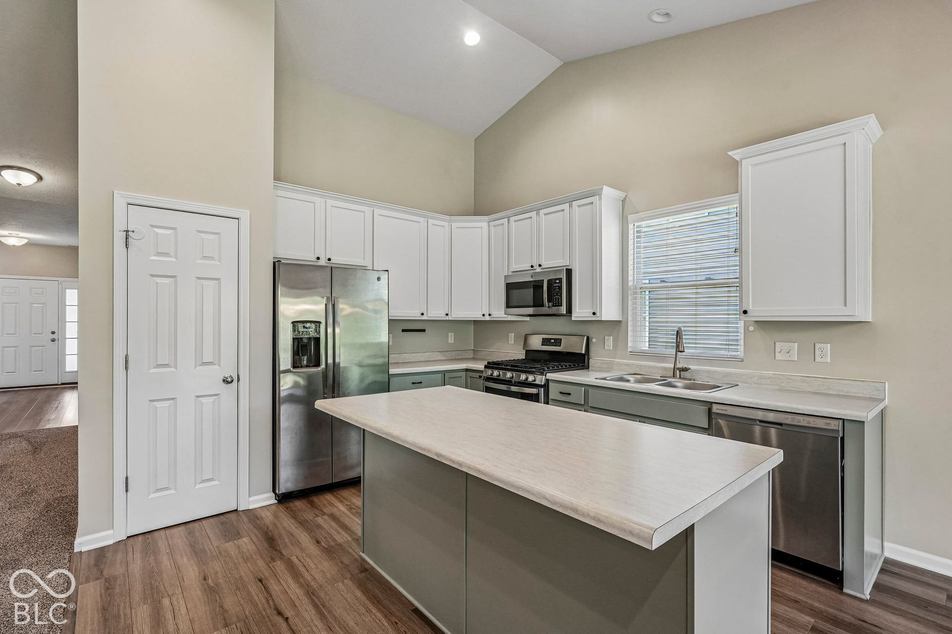 Kitchen featuring vaulted ceiling, white cabinetry, stainless steel appliances, central island, and wood-finish flooring