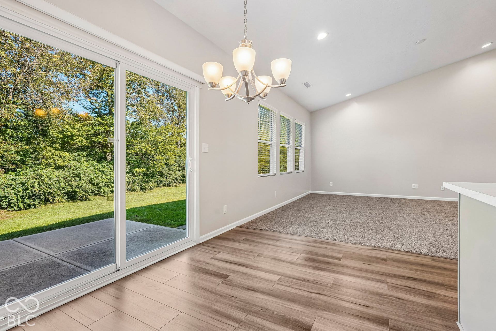 Wood-finish flooring, sliding glass patio door, chandelier, recessed lighting, and a vaulted ceiling