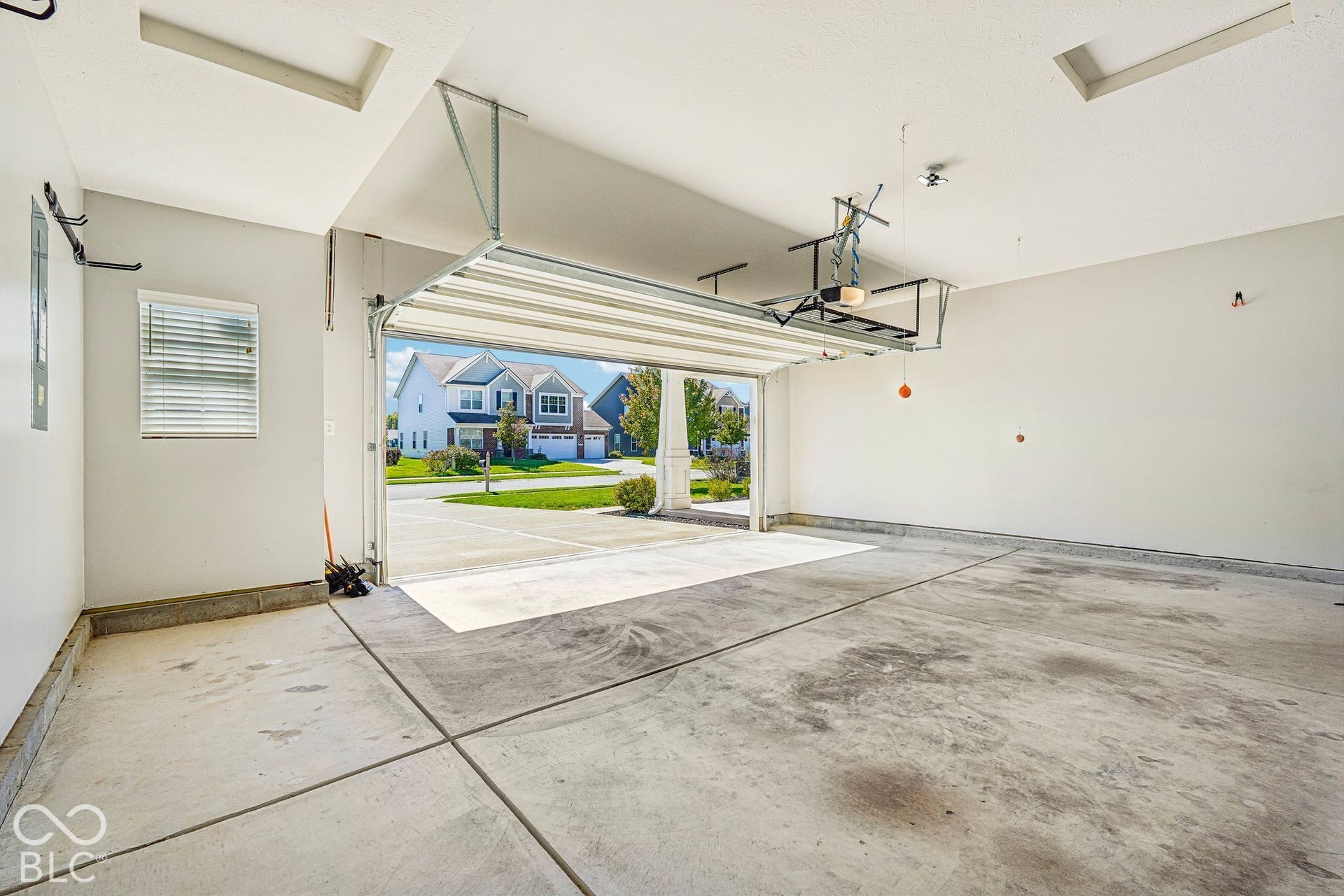 Attached garage with concrete flooring, overhead storage rack, and a window with blinds