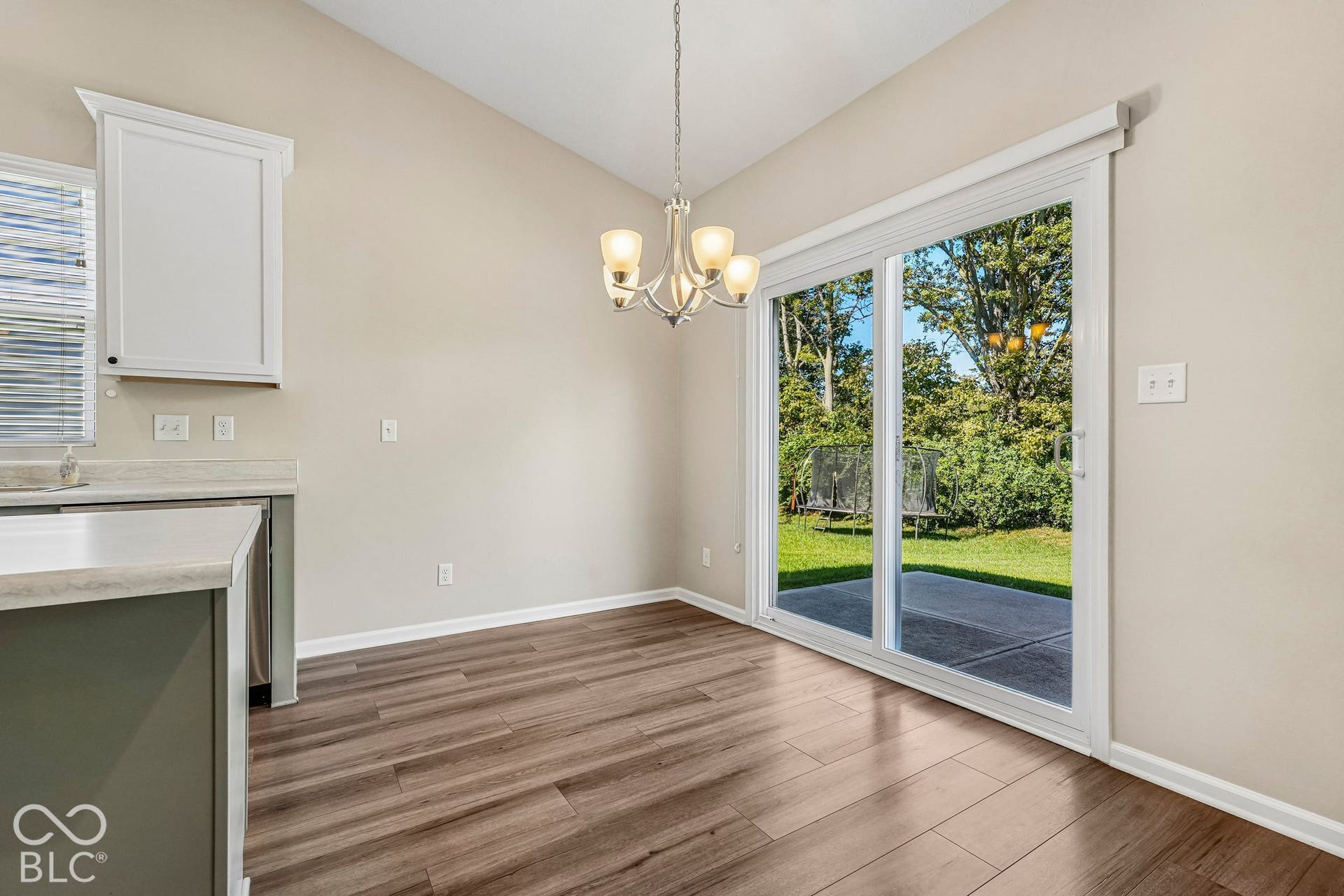 Vaulted ceiling, wood-finish flooring, sliding glass door, contemporary light fixture, and white cabinetry
