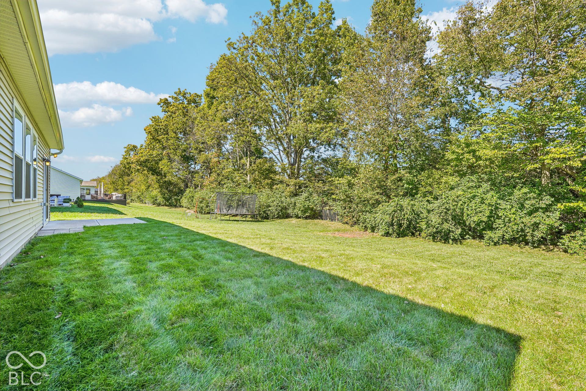 Expansive green lawn, mature perimeter trees, light-colored siding, and concrete patio