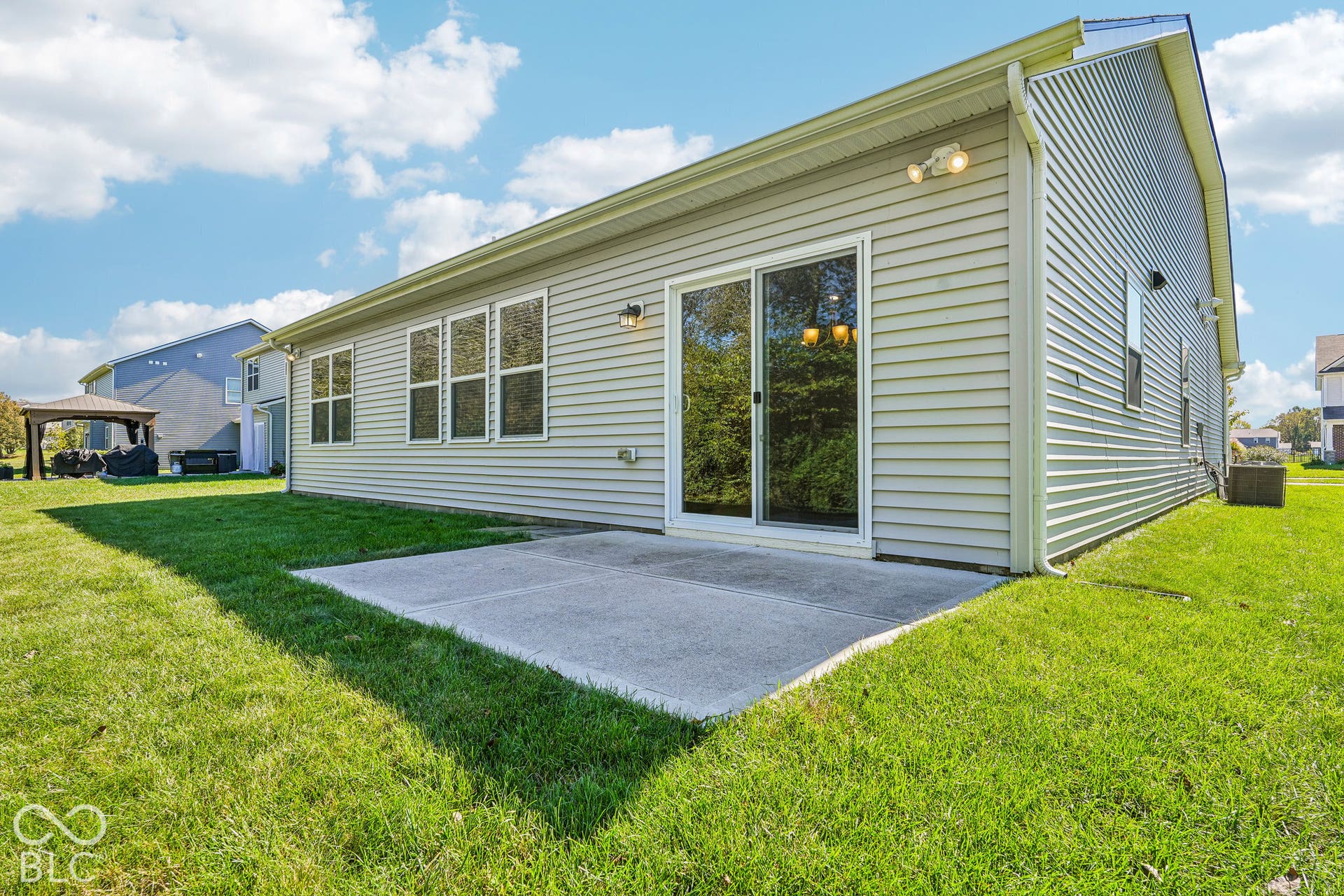 Sliding glass door access to the concrete patio, expansive grassy area, and multiple windows