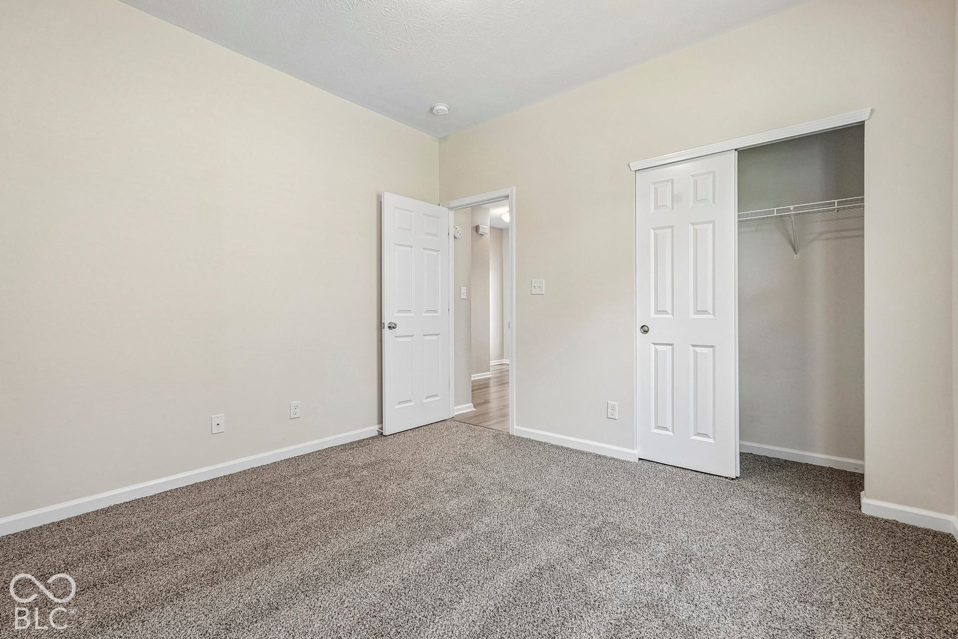 Neutral tone wall paint, textured carpet flooring, white trim, and a built-in closet with wire shelving