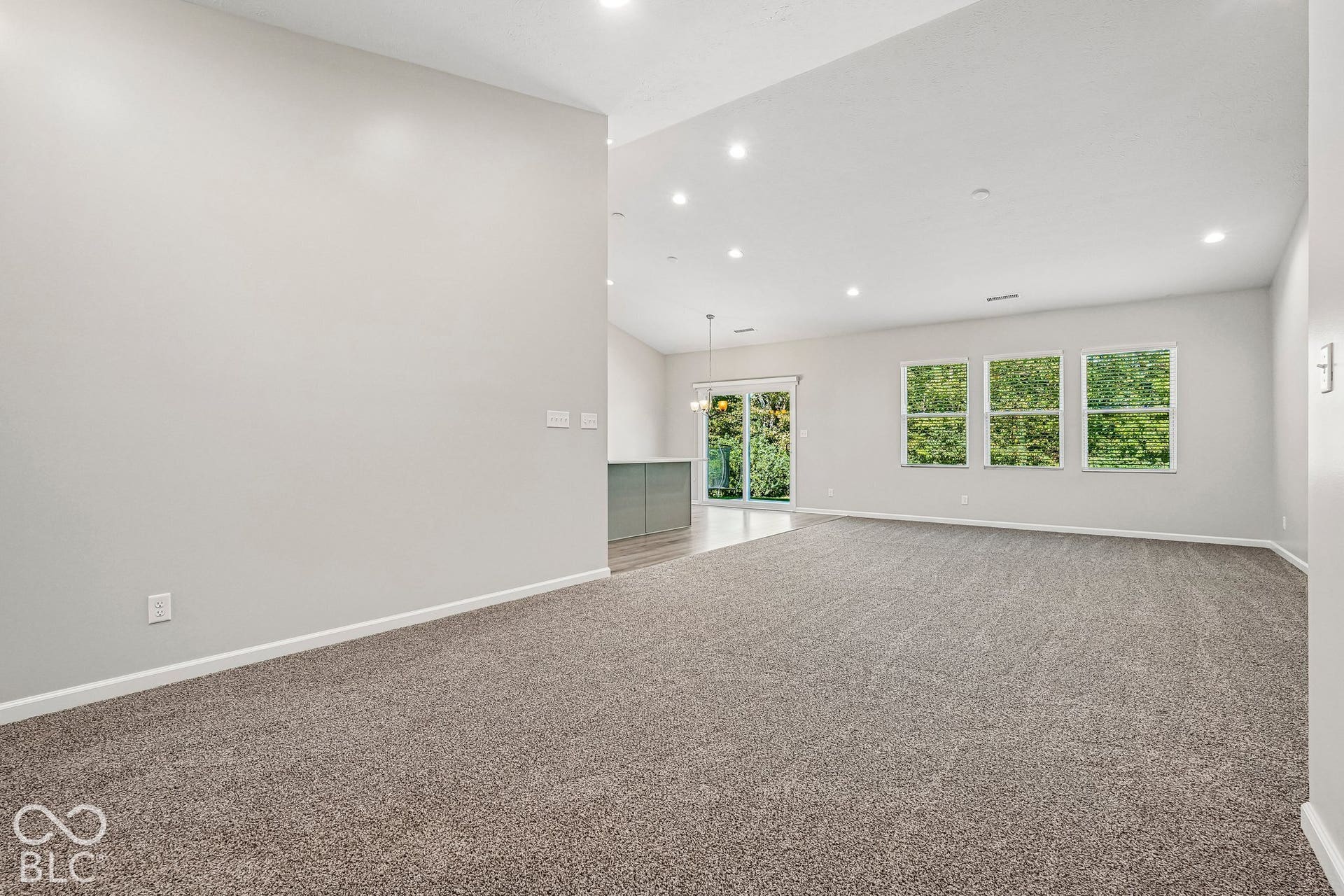 Vaulted ceilings, recessed lighting, large windows, sliding glass door, and neutral carpeting