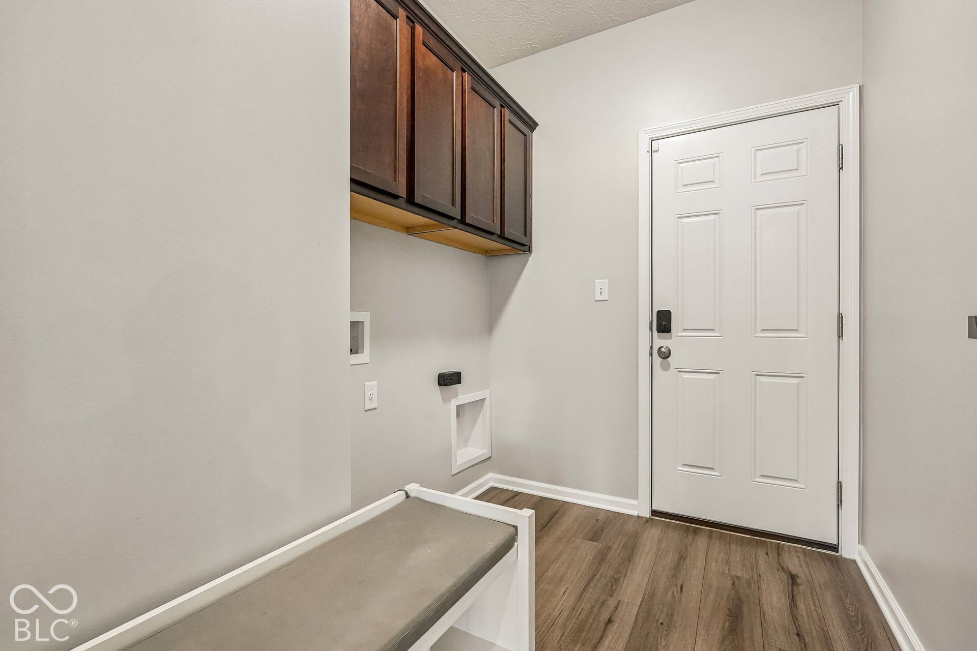 Wood-finish flooring, built-in storage bench, dark wood-finish cabinetry, and a paneled entry door