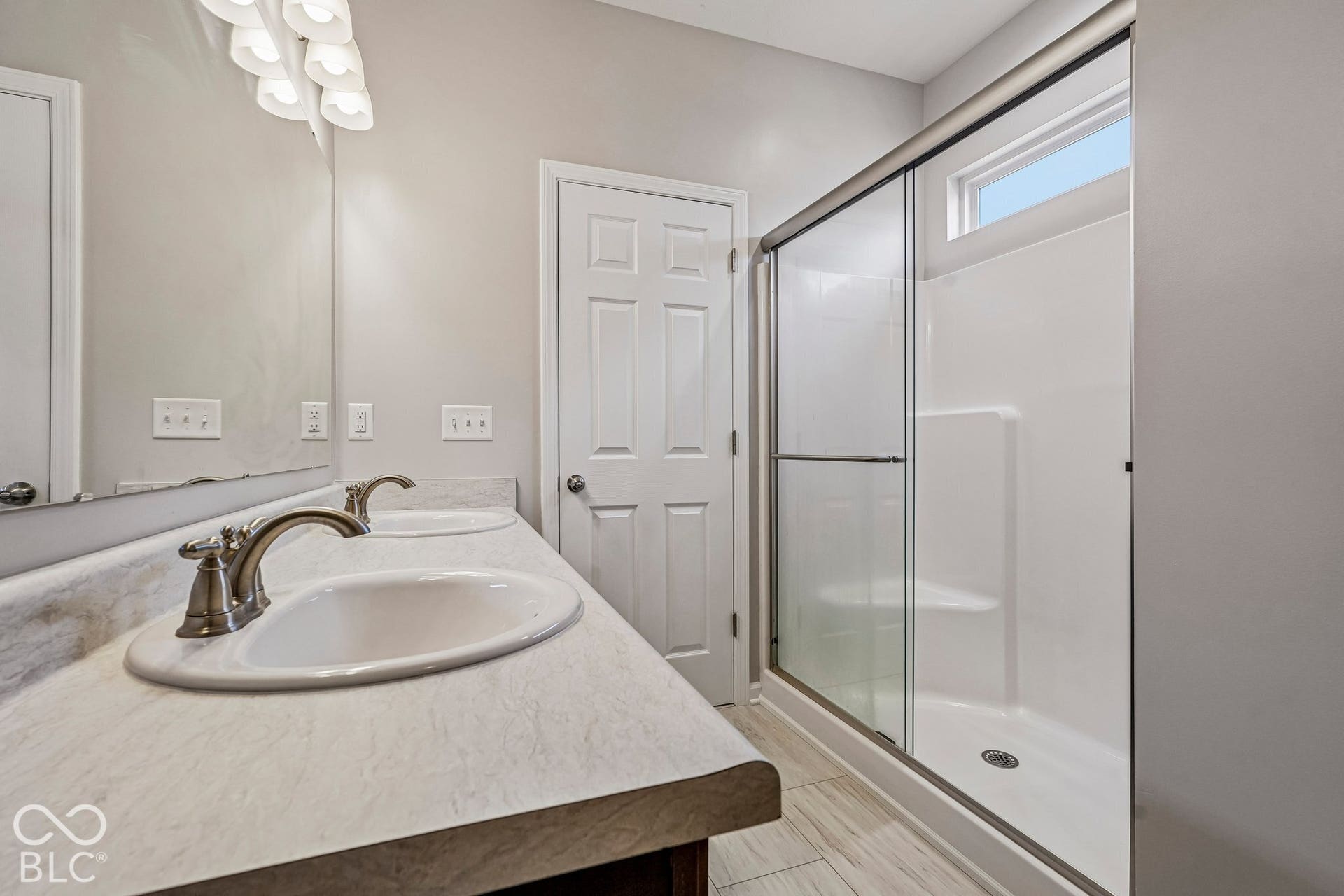 Dual vanity with integrated sinks, brushed nickel fixtures, glass-enclosed shower, transom window, and tile flooring