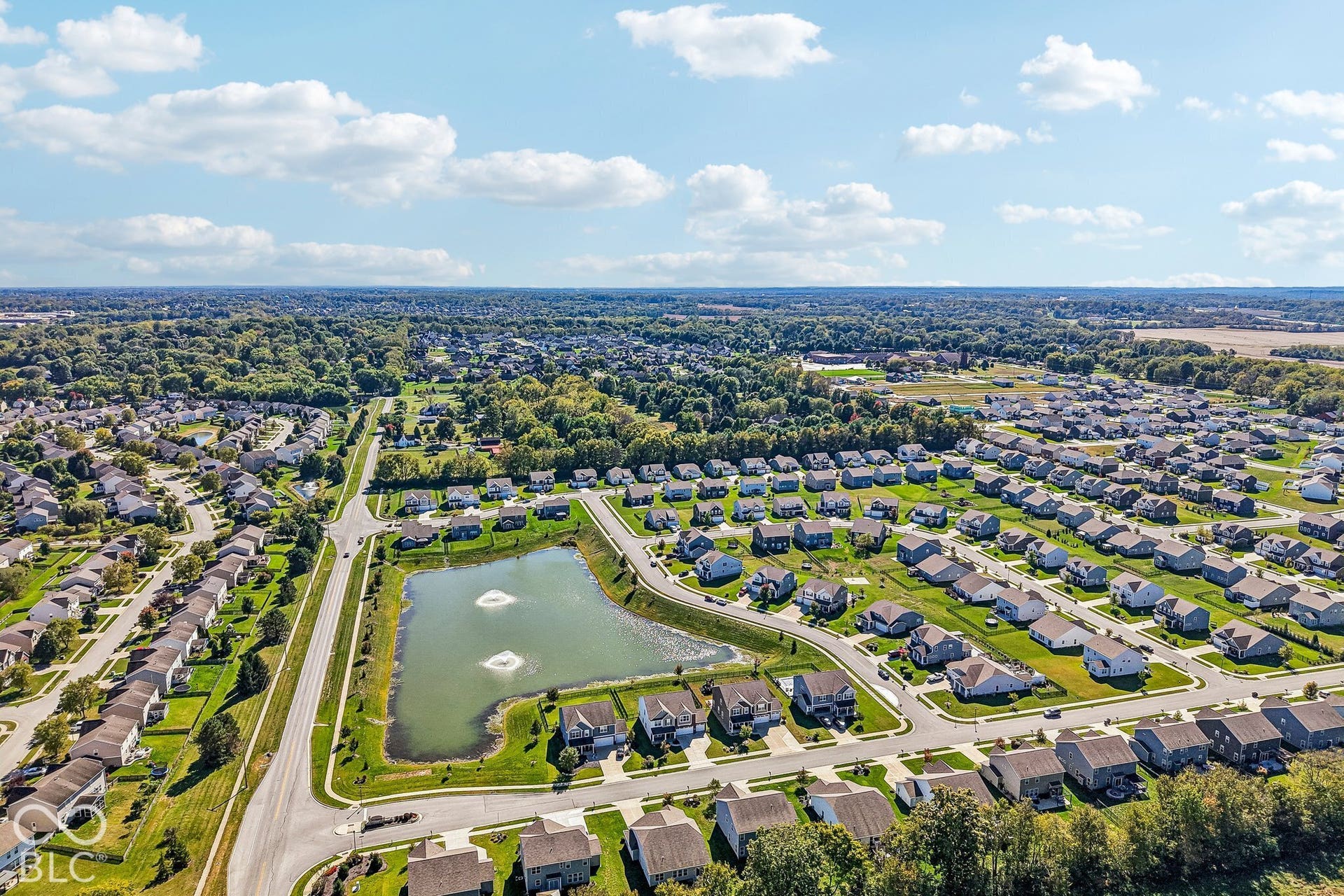 Residential development featuring a central pond with water features, surrounded by detached homes and green spaces