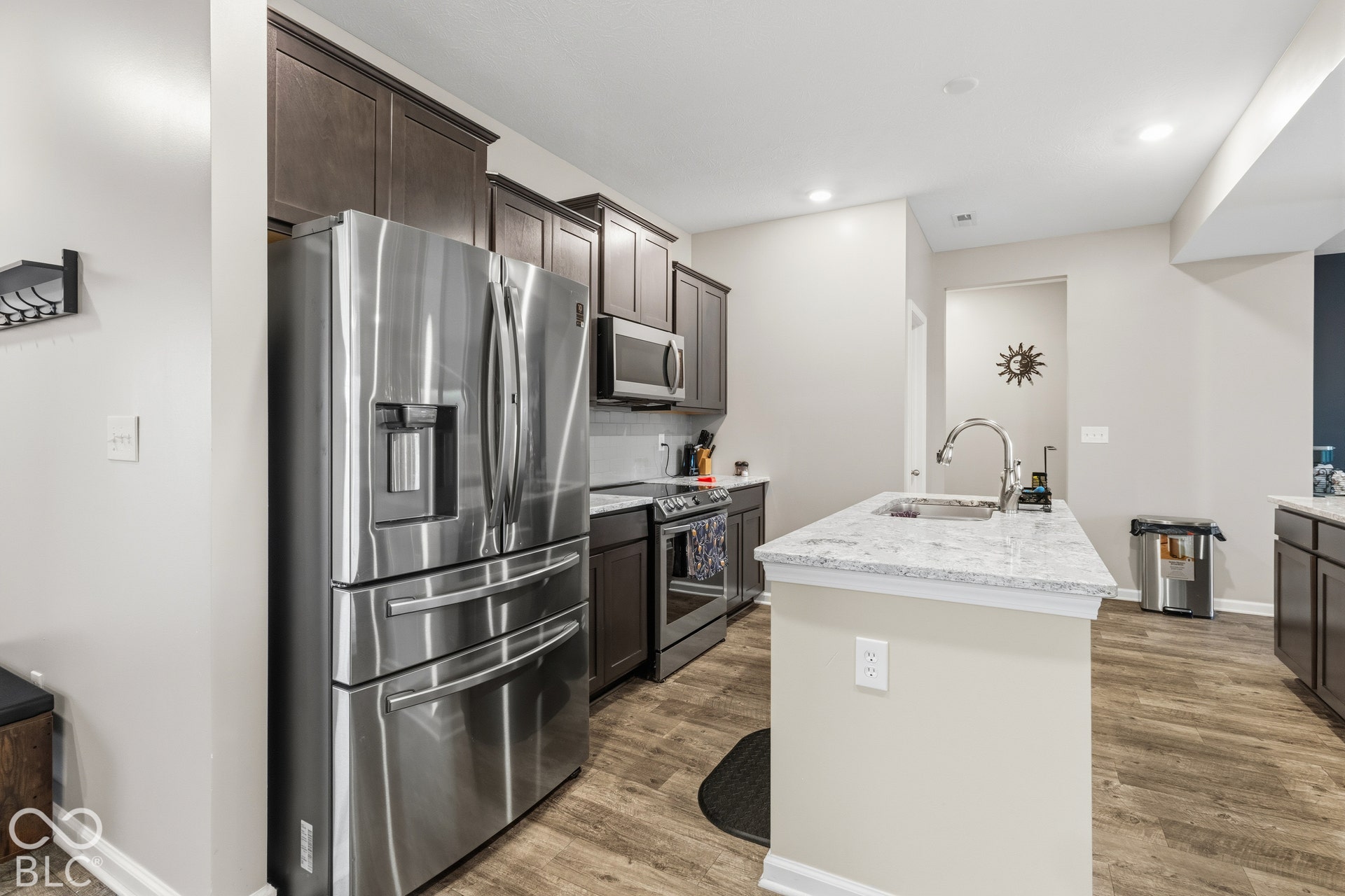 Kitchen featuring stainless steel appliances, dark wood-finish cabinetry, a central island with a sink, light-toned countertops, and wood-finish flooring