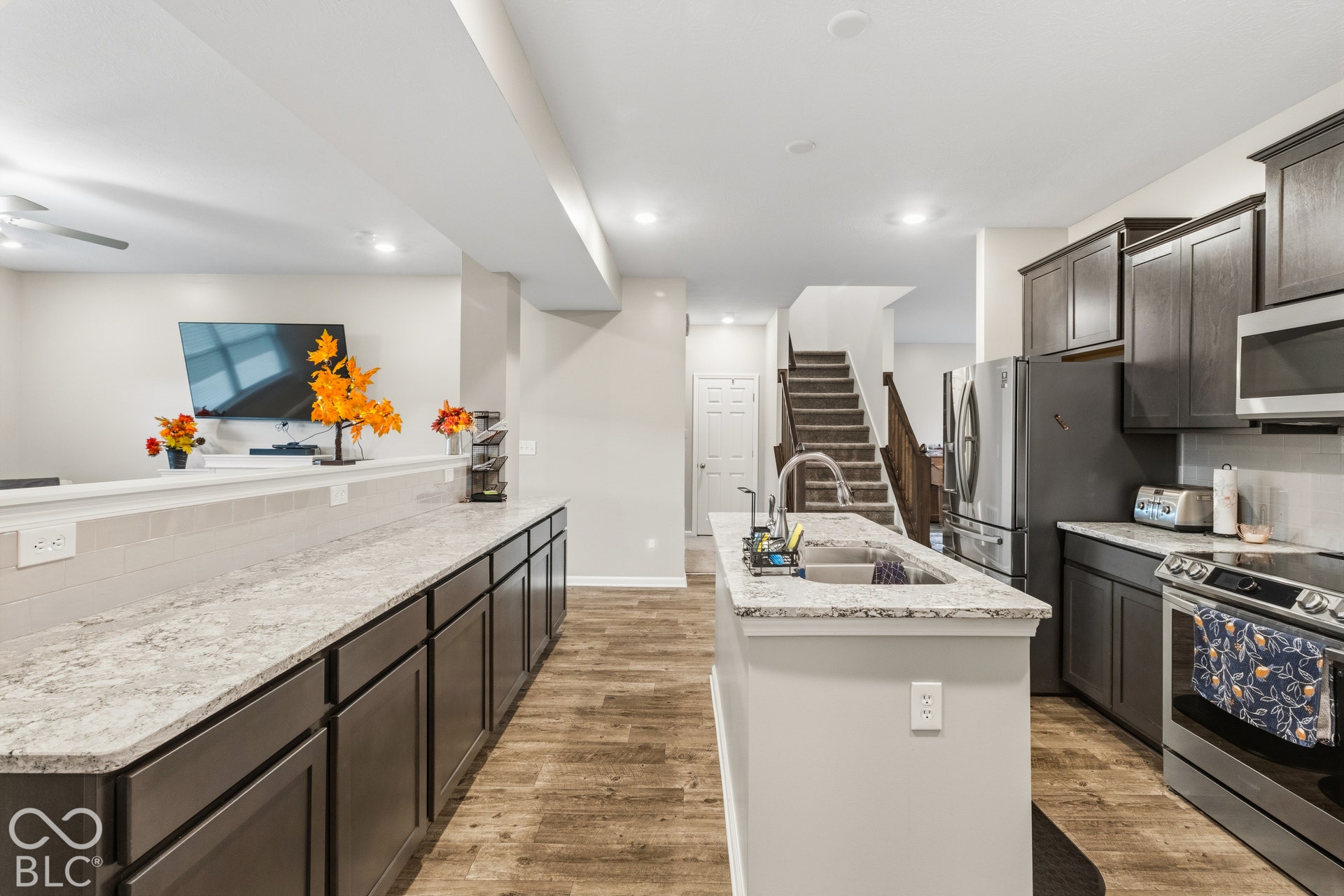 Spacious kitchen featuring an island with an undermount sink, stainless steel appliances, dark wood-finish cabinetry, light-toned countertops, and wood-finish flooring
