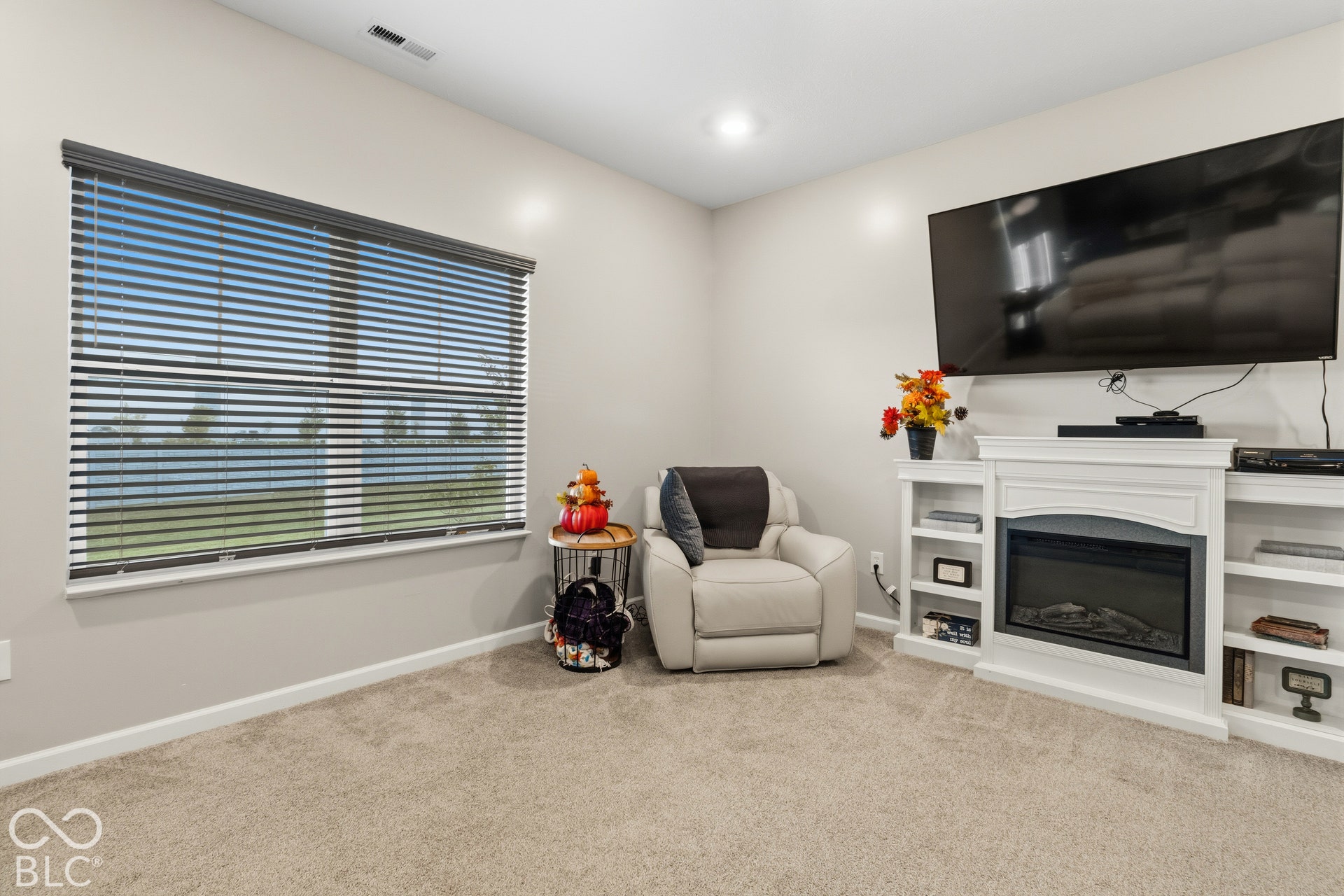 Recessed lighting, wall-mounted television, built-in electric fireplace with mantel, built-in shelving, and carpet flooring