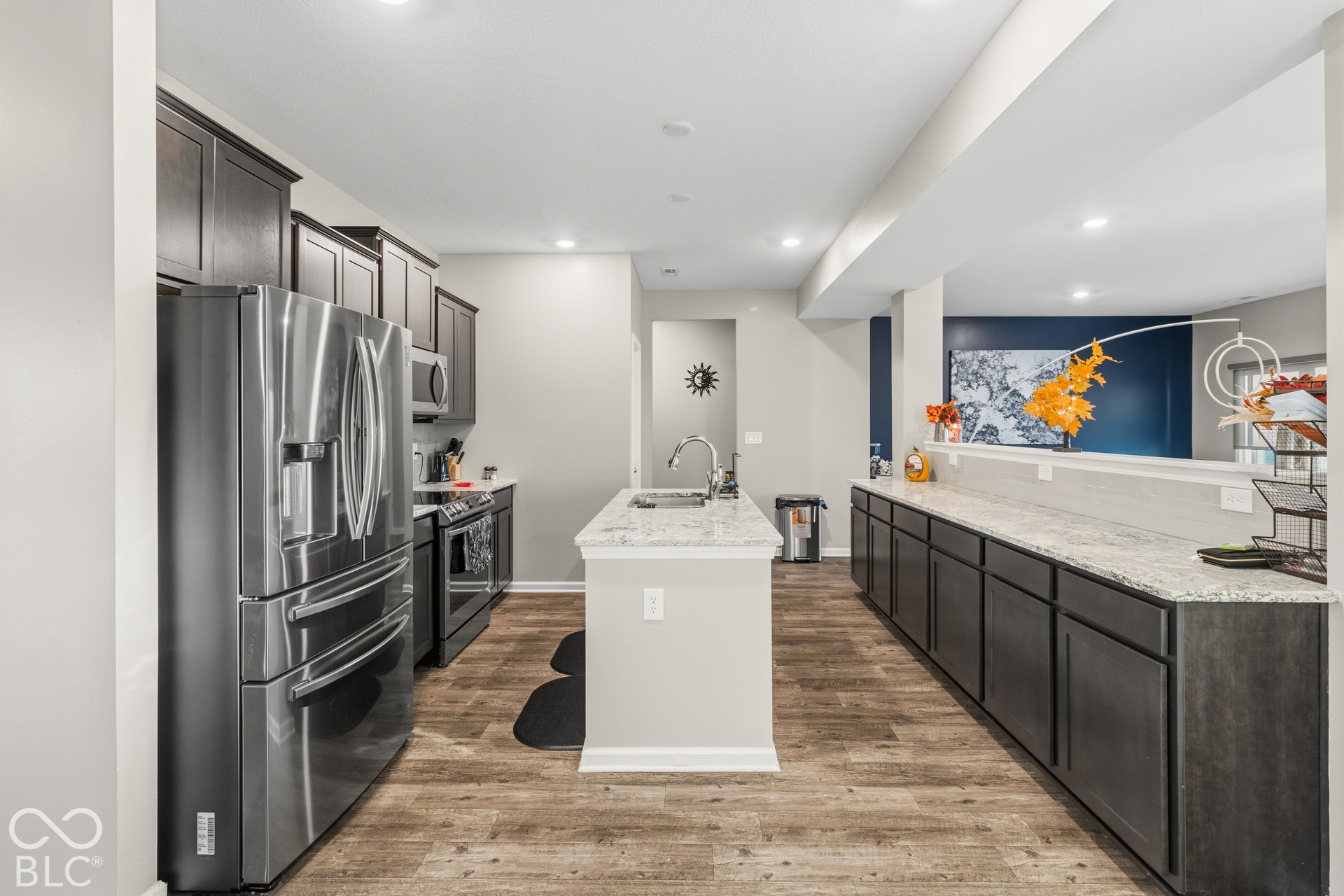 Kitchen featuring dark cabinetry, stainless steel appliances, a center island with a sink, quartz countertops, and wood-finish flooring