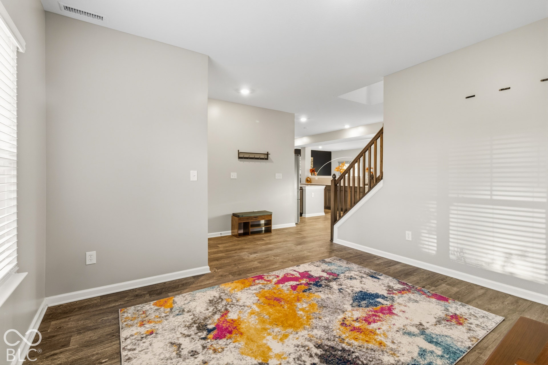 Recessed lighting, wood-finish flooring, white window blinds, and a wood-toned staircase with balusters