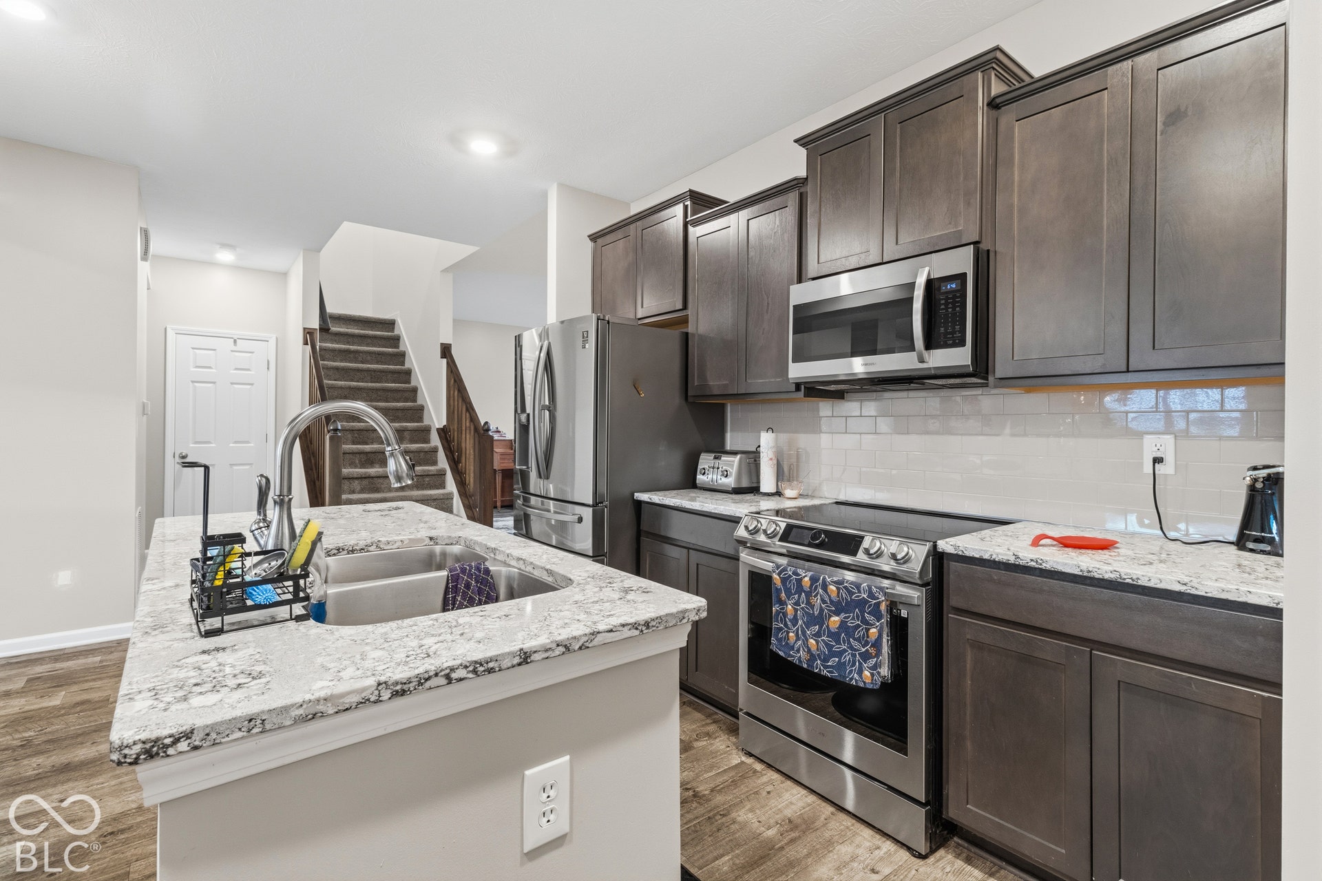 Kitchen featuring stainless steel appliances, dark wood-finish cabinetry, light-toned countertops, a subway tile backsplash, and wood-finish flooring