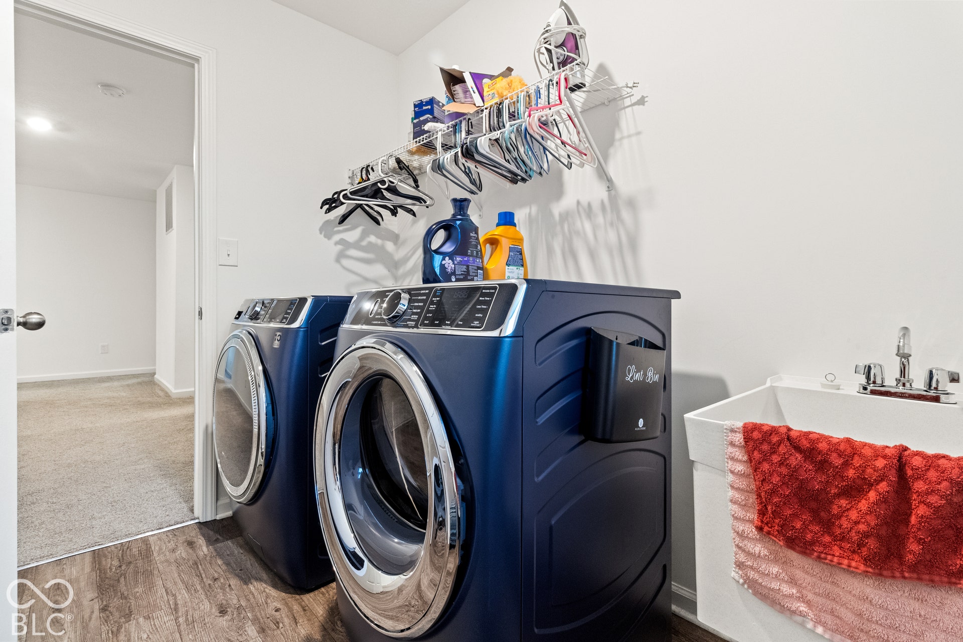 Laundry area featuring wood-finish flooring, a utility sink with a chrome faucet, and white walls