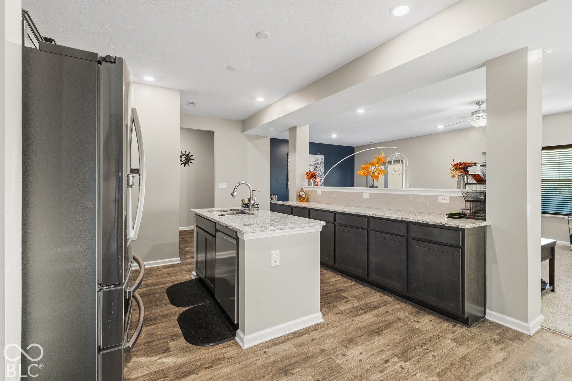 Modern kitchen featuring an island with a stainless steel sink, upgraded quartz countertops, wood-finish flooring, dark cabinetry, and recessed lighting
