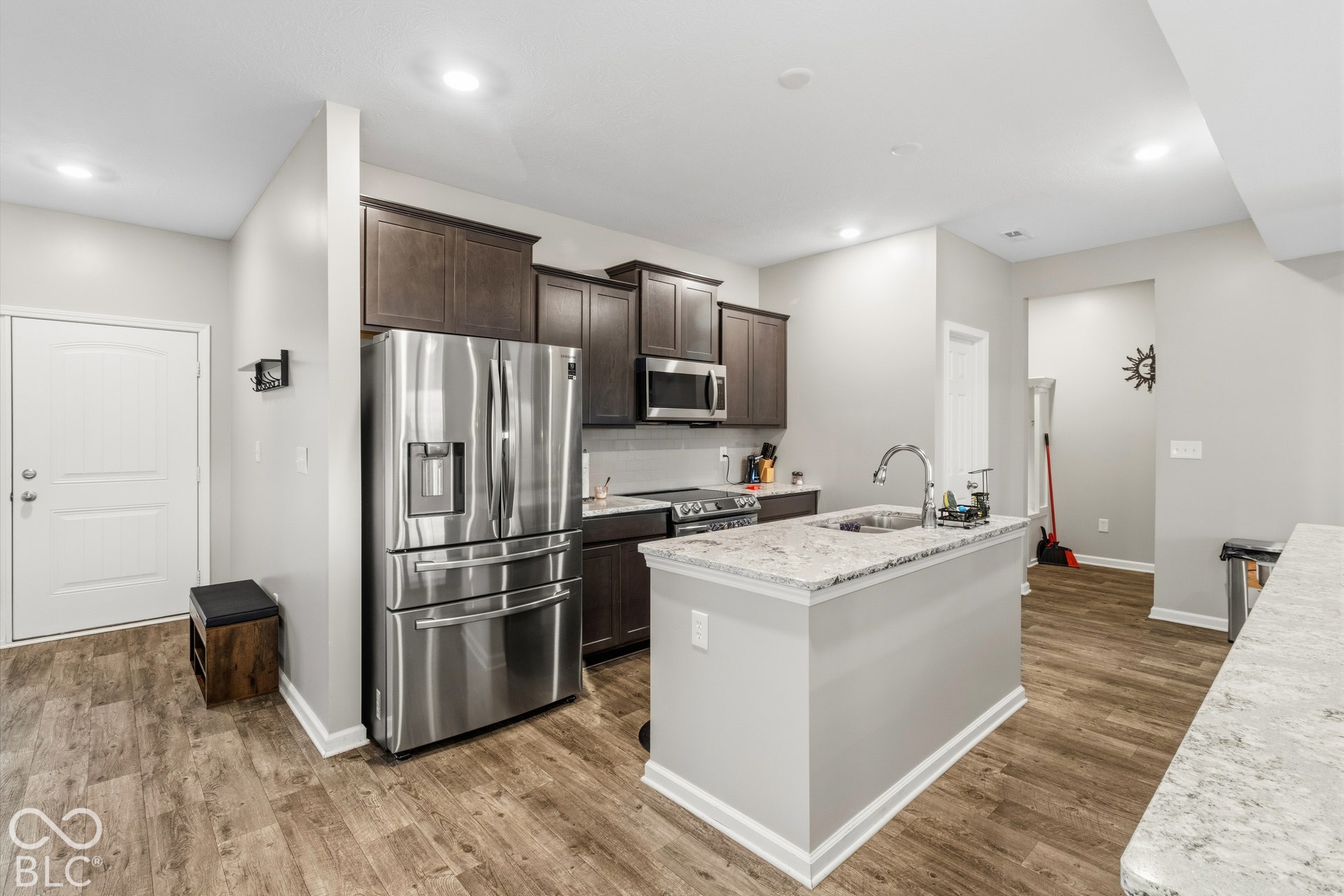 Kitchen featuring wood-finish flooring, dark wood cabinetry, stainless steel appliances, and a central island with a sink and quartz countertop