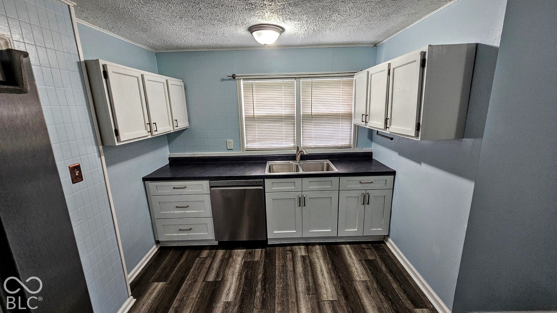 104 E State Street, New Ross, IN 47968 Kitchen featuring a stainless steel dishwasher, dual basin sink, wood-finish flooring, and white cabinetry with dark hardware