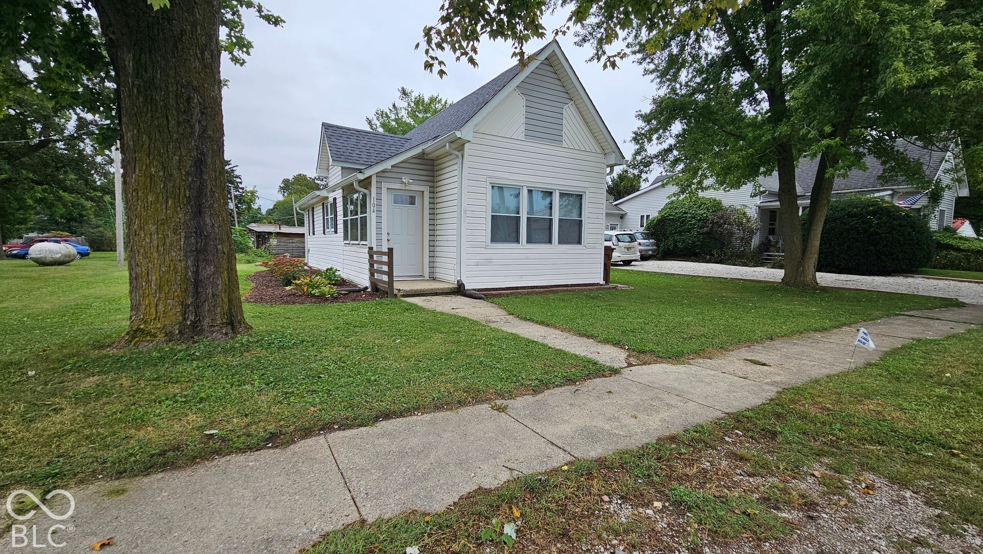 104 E State Street, New Ross, IN 47968 White siding exterior with a dark shingle roof, established landscaping, and a concrete walkway