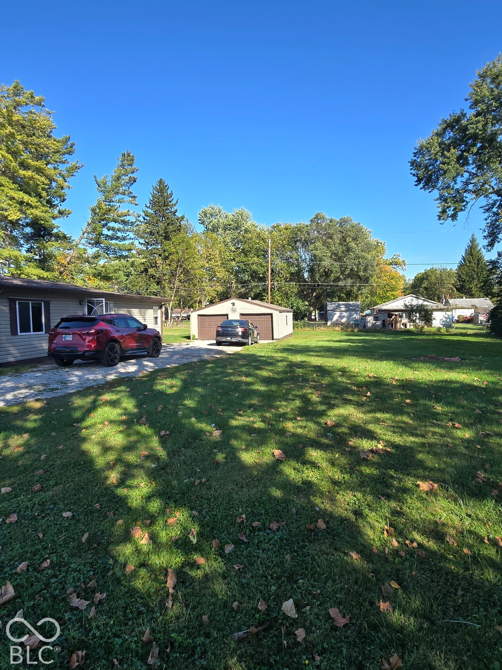 Expansive lawn area with mature trees and a gravel driveway