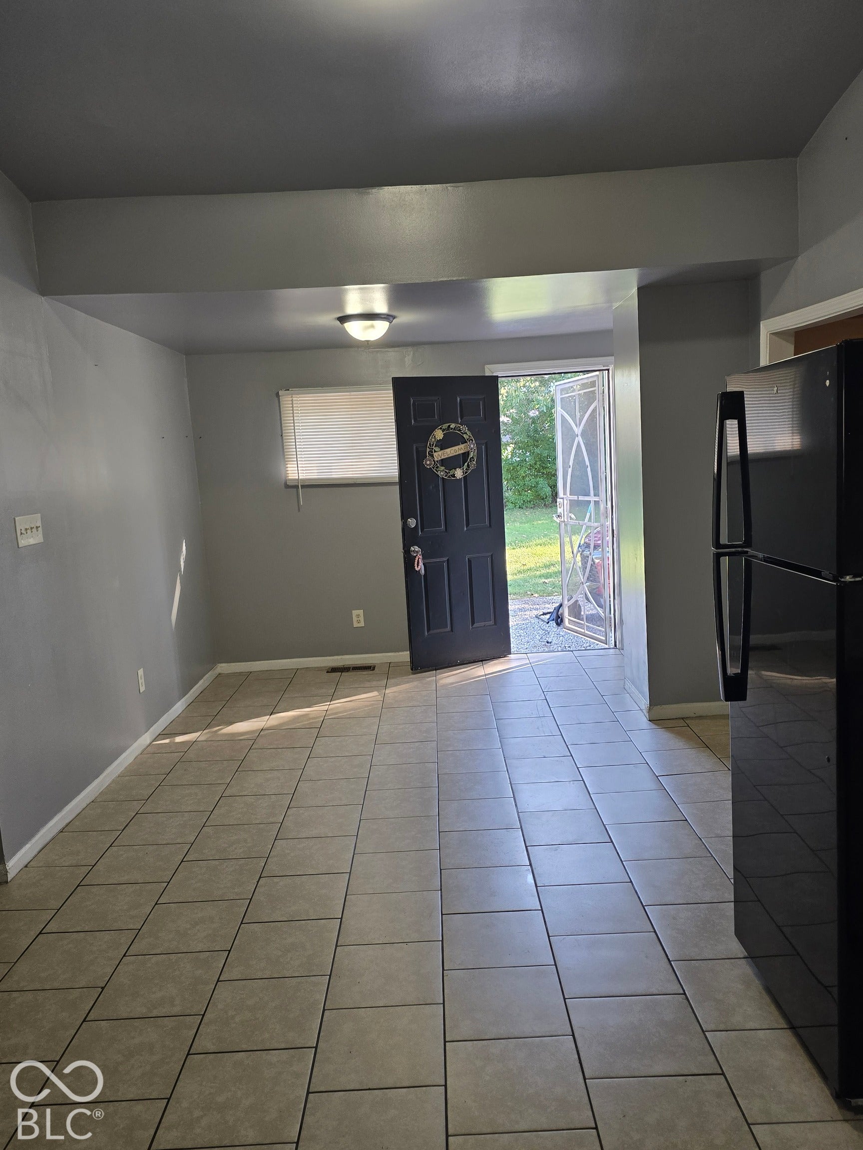 Ceramic tile flooring, neutral wall color, overhead lighting, and an exterior door with security screen