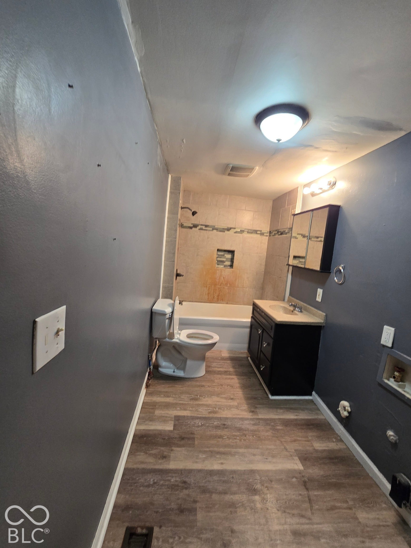 Full bathroom featuring a white tub, dark wood-finish vanity with countertop, wood-finish flooring, and wall-mounted medicine cabinet