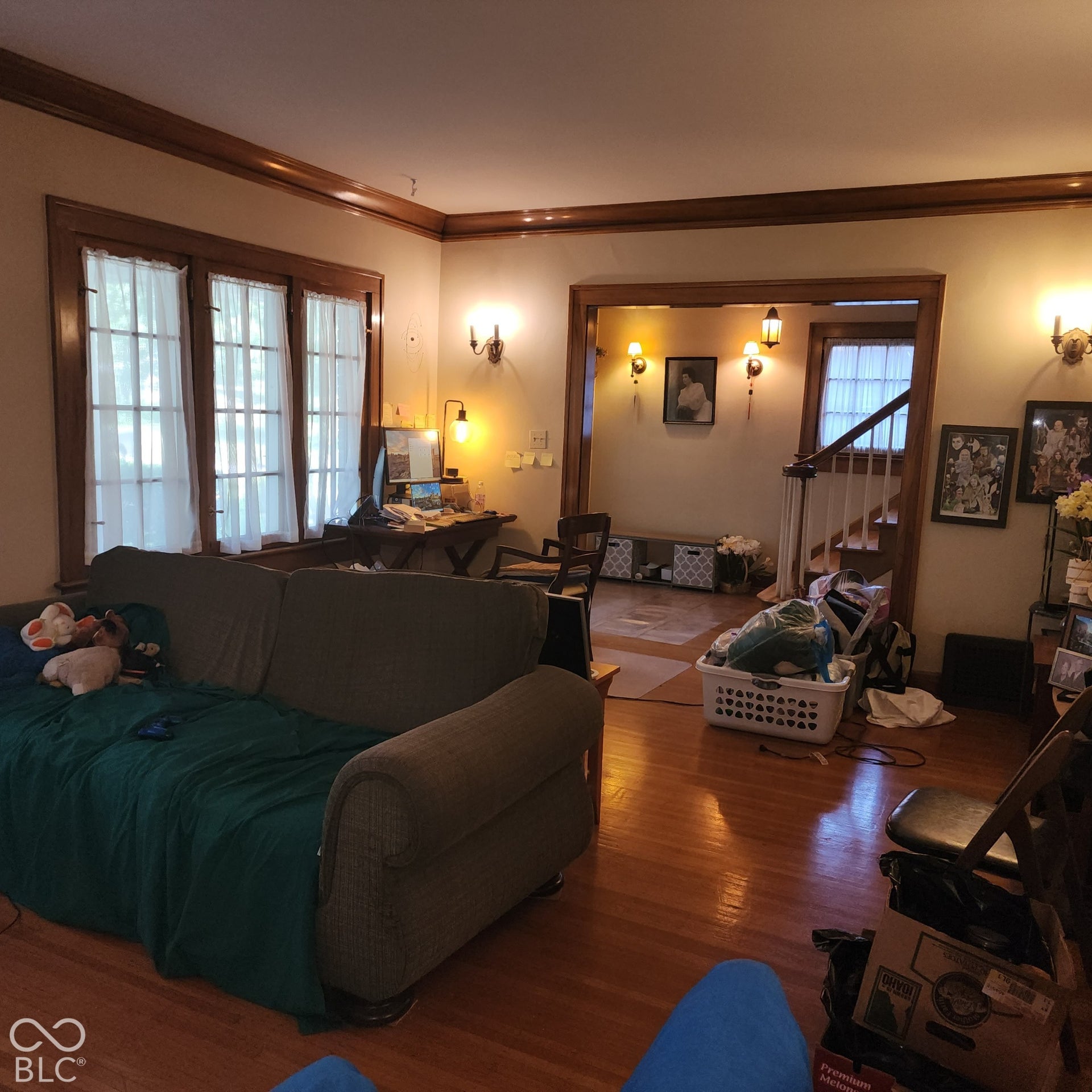 Hardwood flooring, wood trim accents, multiple wall sconces, large windows, and a staircase with wood railing