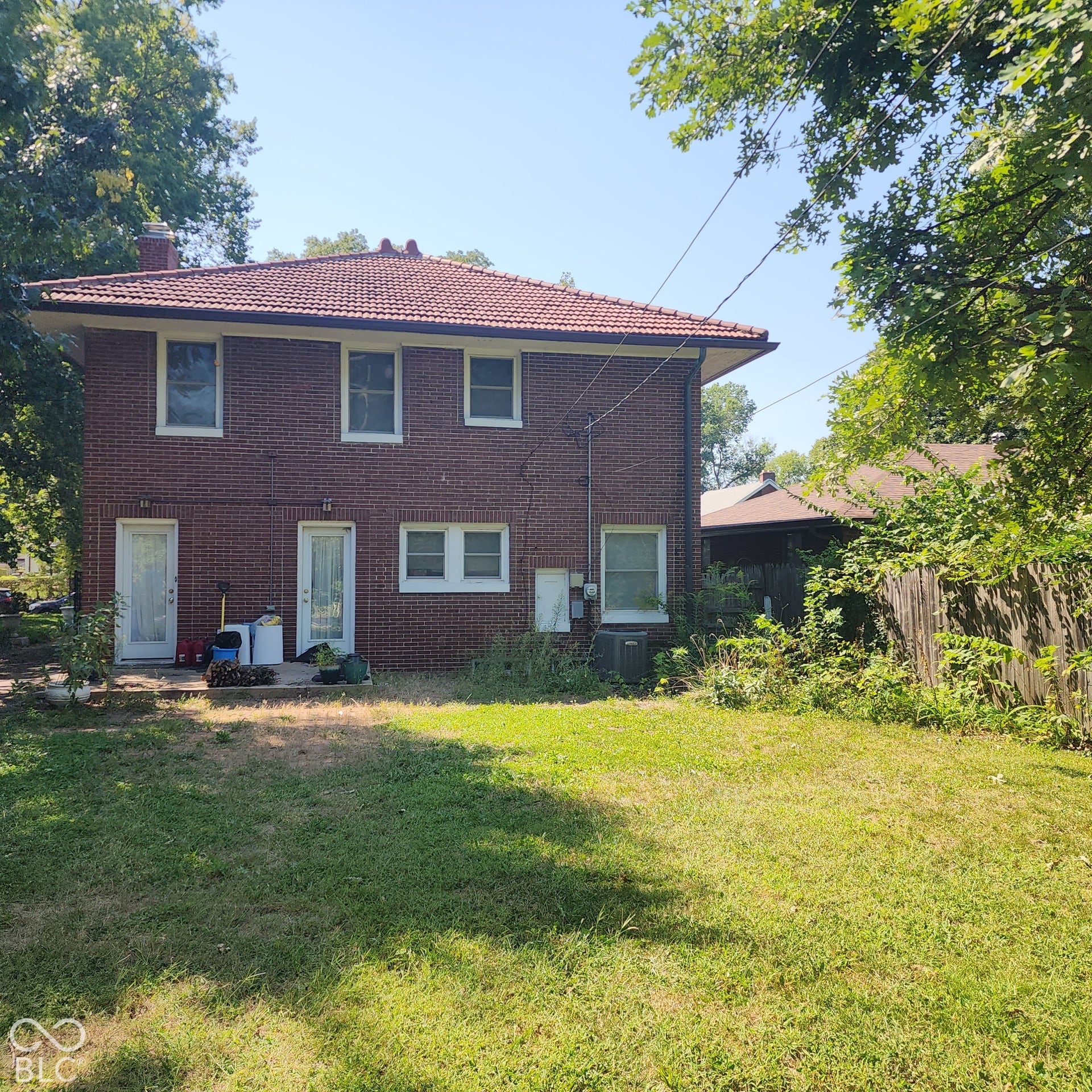 Brick exterior featuring a terracotta tile roof, multiple windows, and a grassy backyard