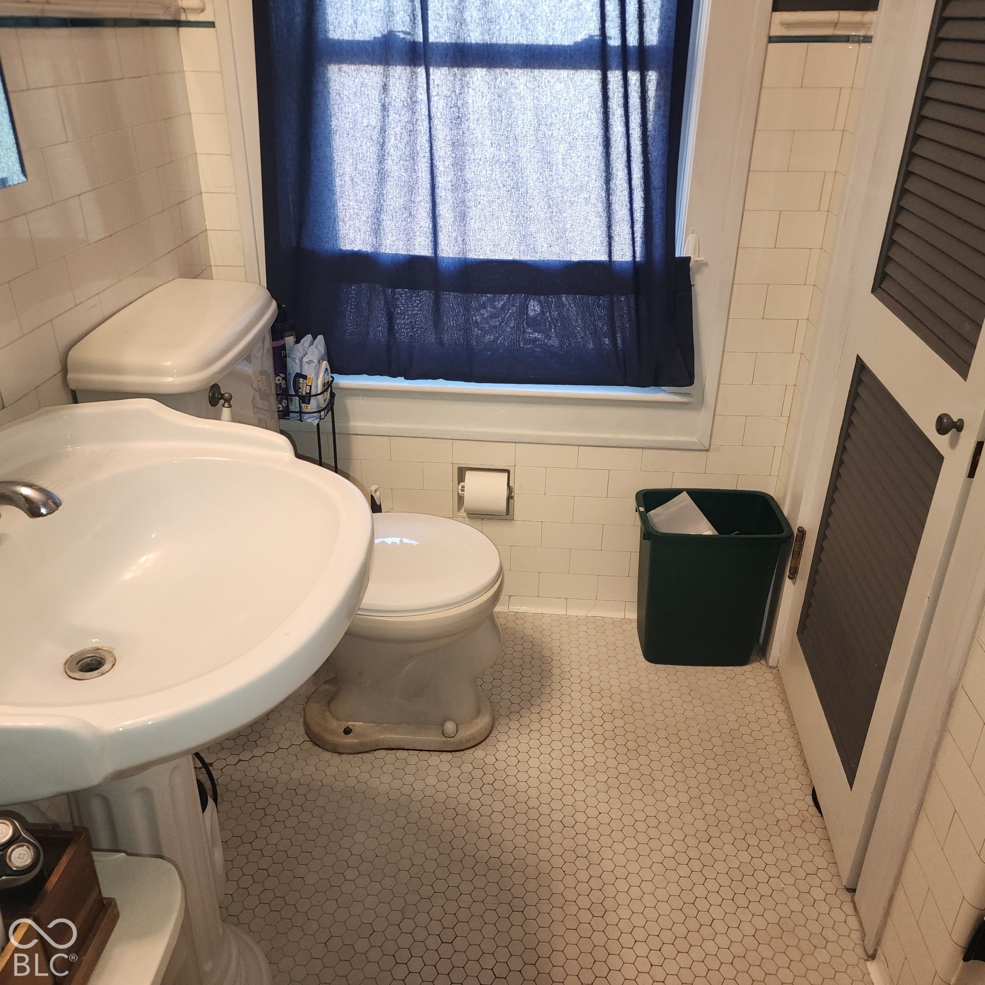 White hexagonal tile flooring, pedestal sink, window, louvered door, white wall tiling